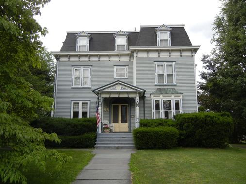 Gray two-story house with a front porch, steps, and manicured lawn surrounded by trees