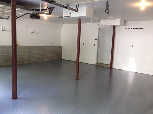 Empty basement with gray floor, white walls, exposed pipes, and red support poles.