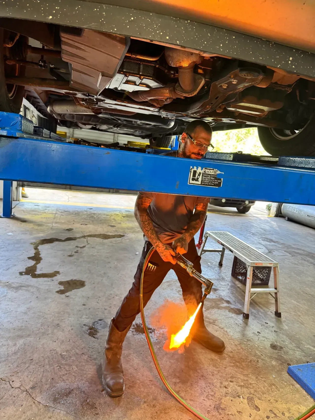 Mechanic welding under a raised car on a blue lift, sparks flying in a garage | RMP Auto