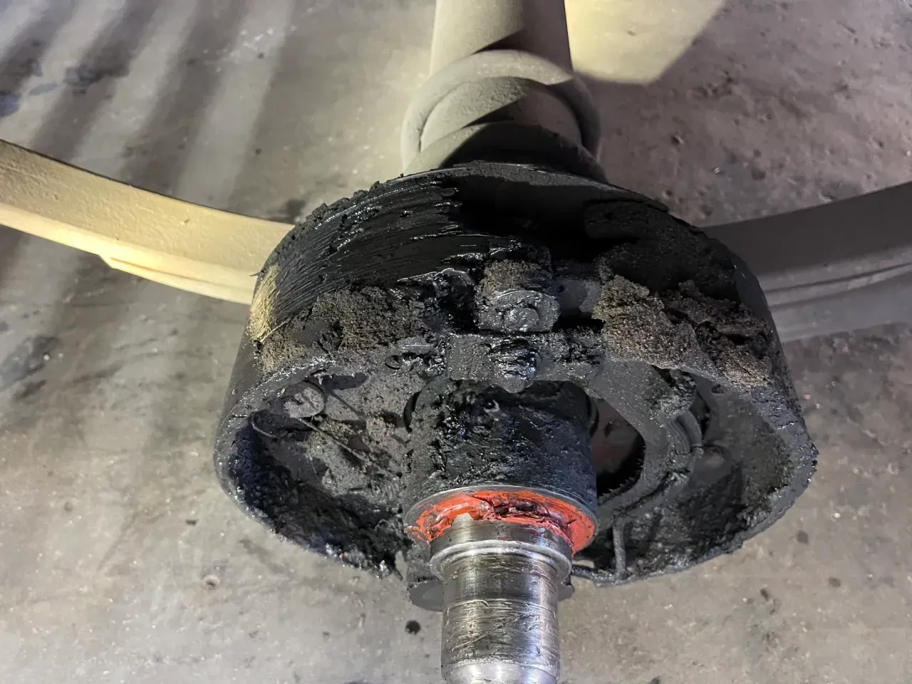 Close-up of a worn black wheel hub and axle assembly with grease residue on a garage floor | RMP Auto