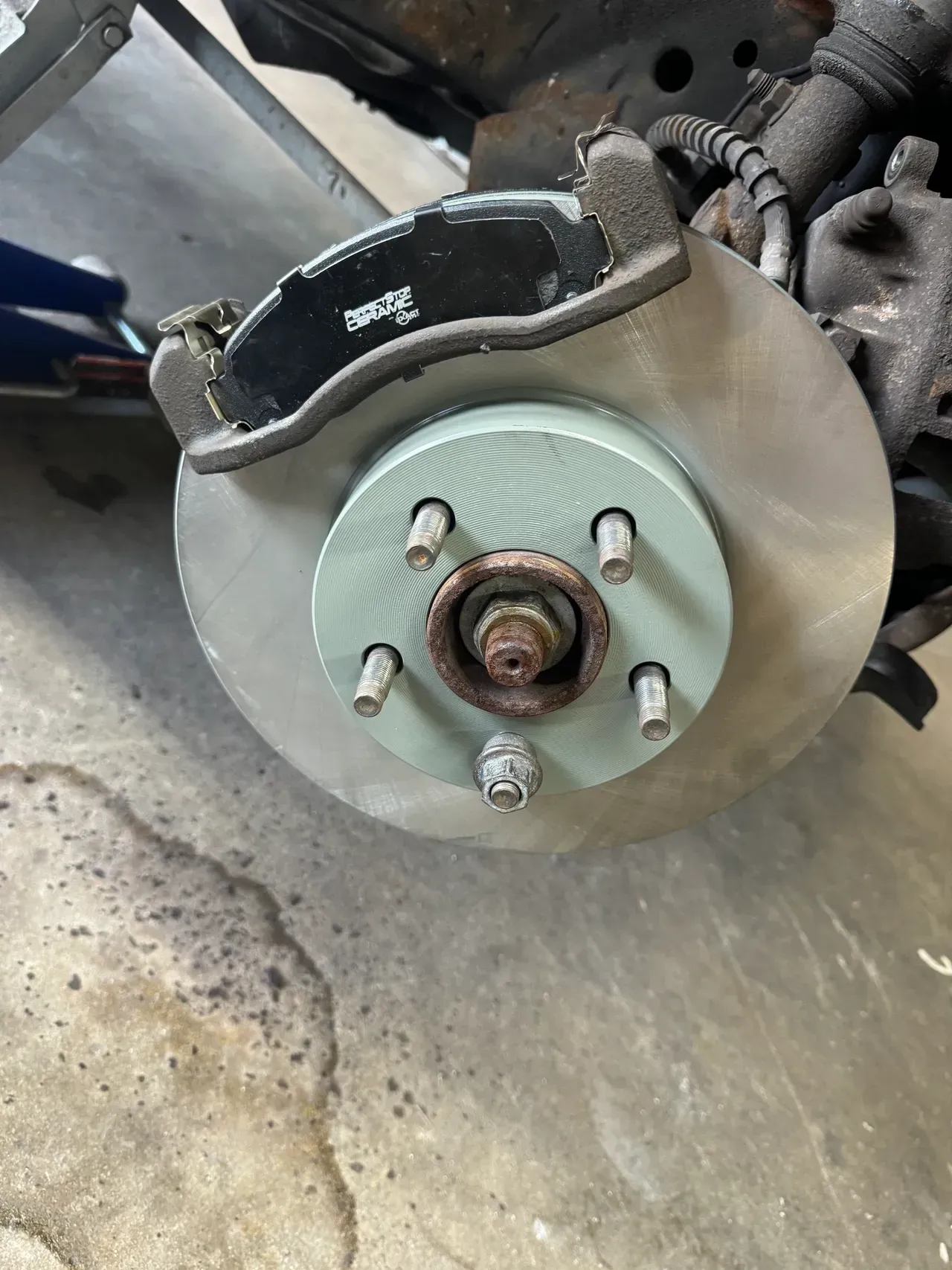Close-up of a car brake rotor and caliper mounted on a wheel hub in a garage. | RMP Auto