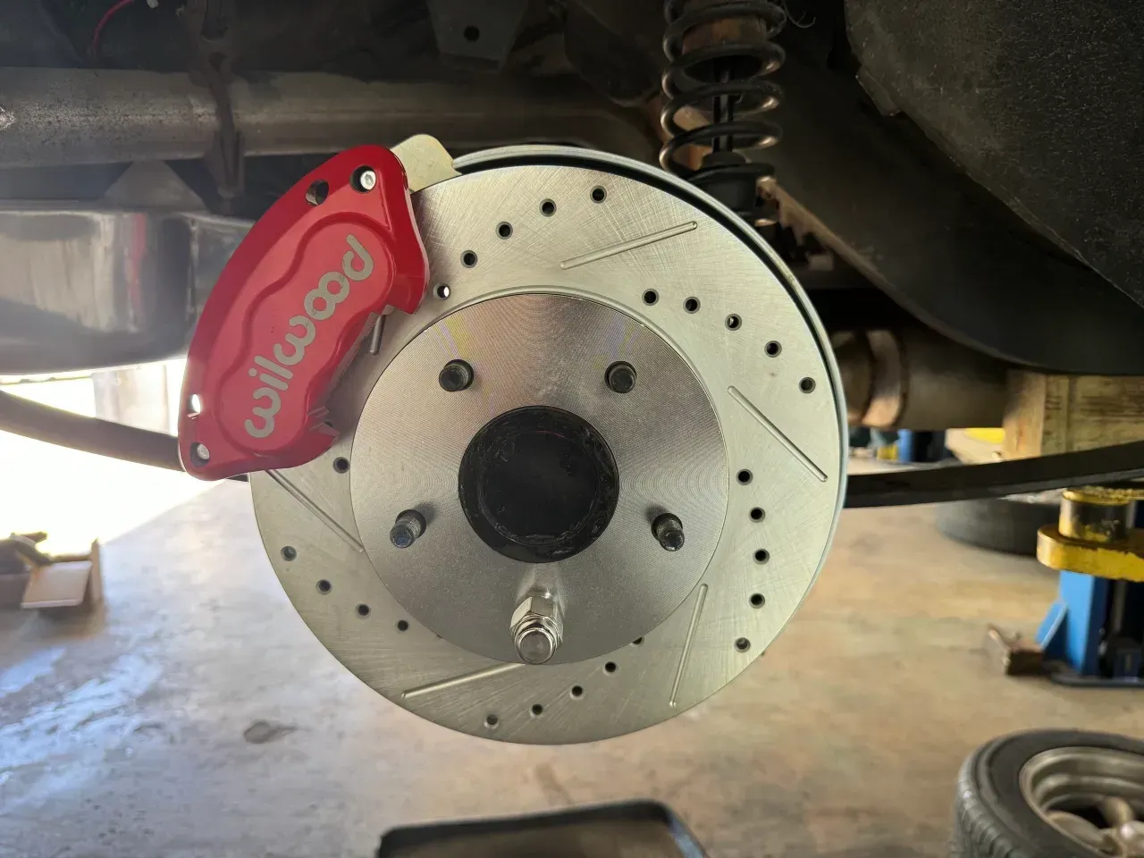 Close-up of a car brake rotor with a red Wilwood caliper under the vehicle. | RMP Auto