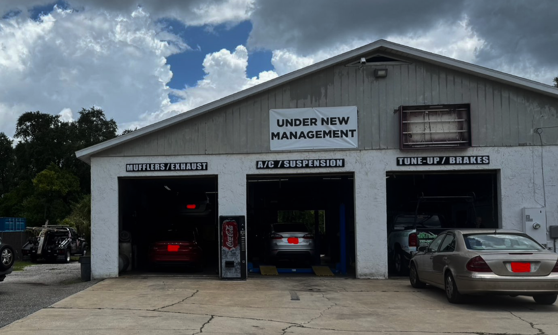 Small auto repair shop with three service bays and cars parked outside under a cloudy sky. | RMP Auto