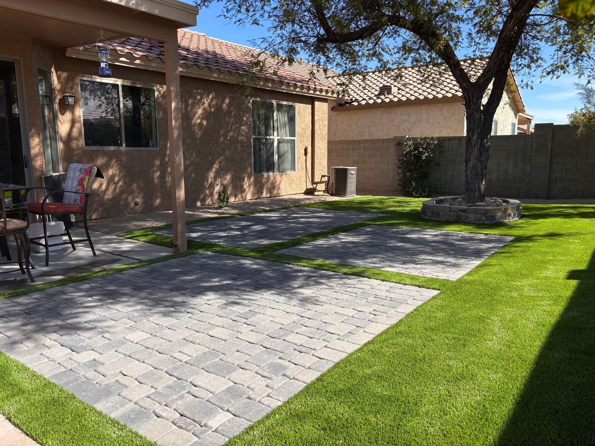 Backyard patio with pavers, lawn, and a brick house under sunny skies