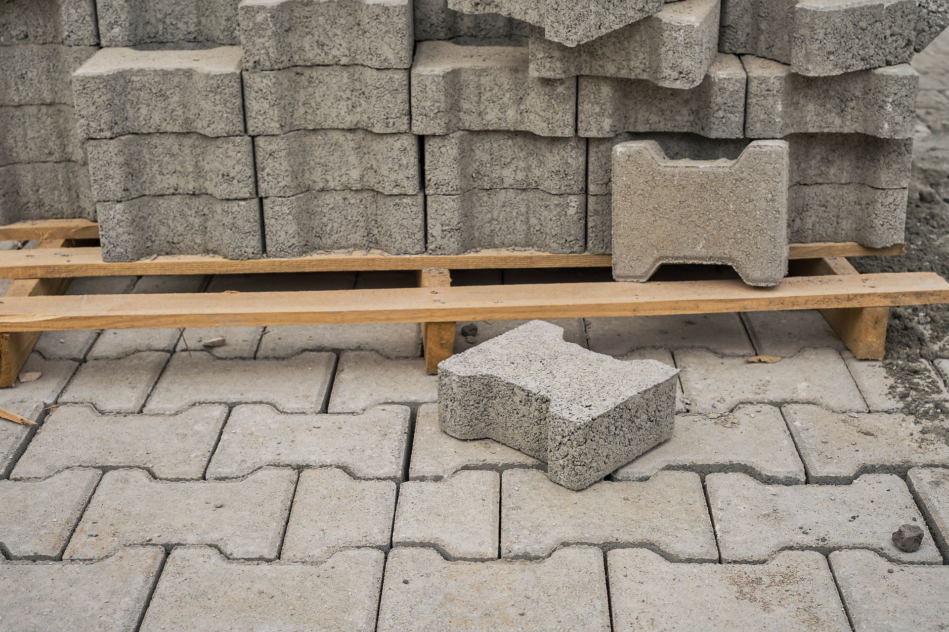 Stacked gray paving blocks on pallets, with one loose block on the ground in front.
