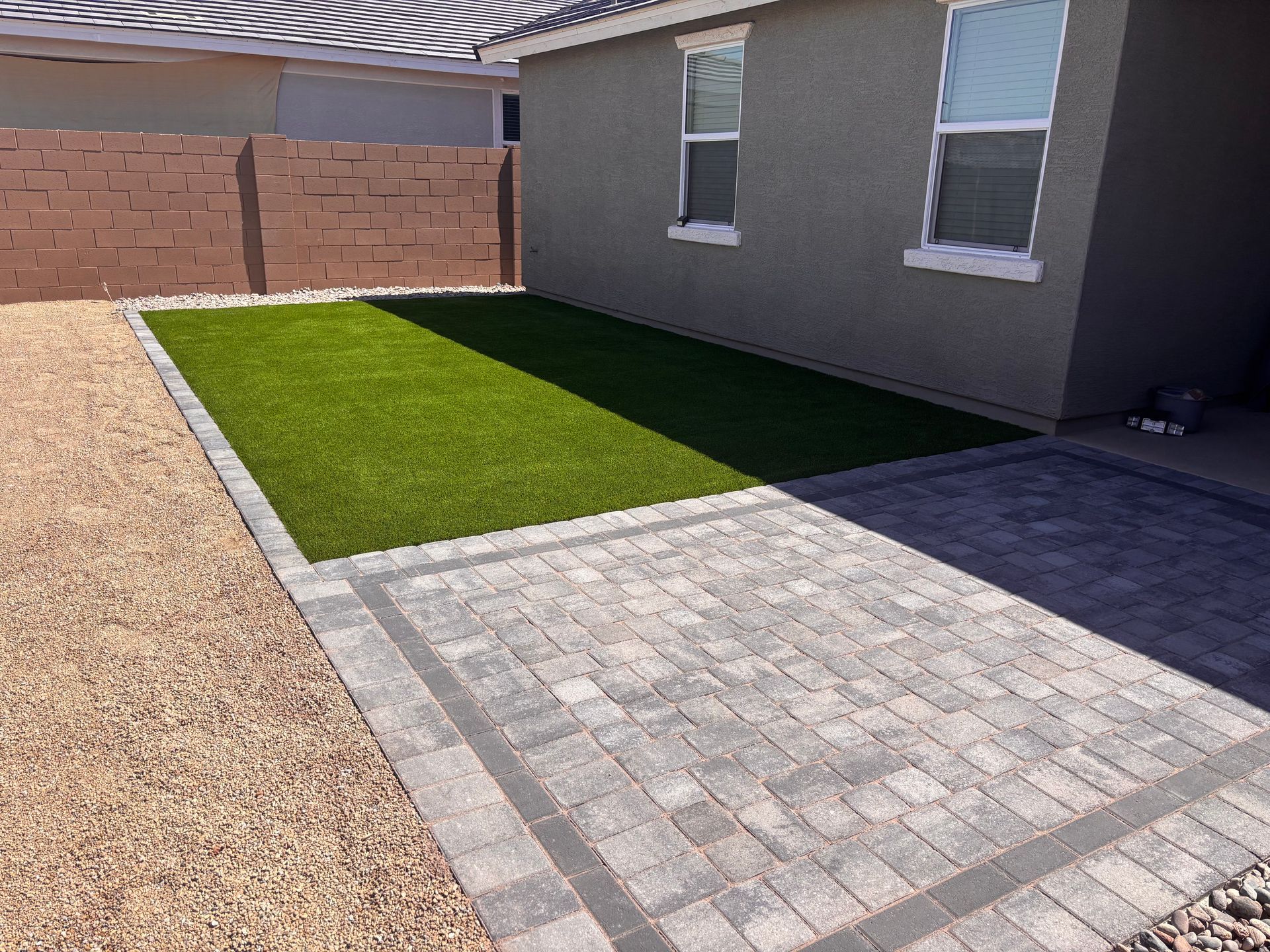 Backyard with paver patio, artificial grass, gravel landscaping, and block wall