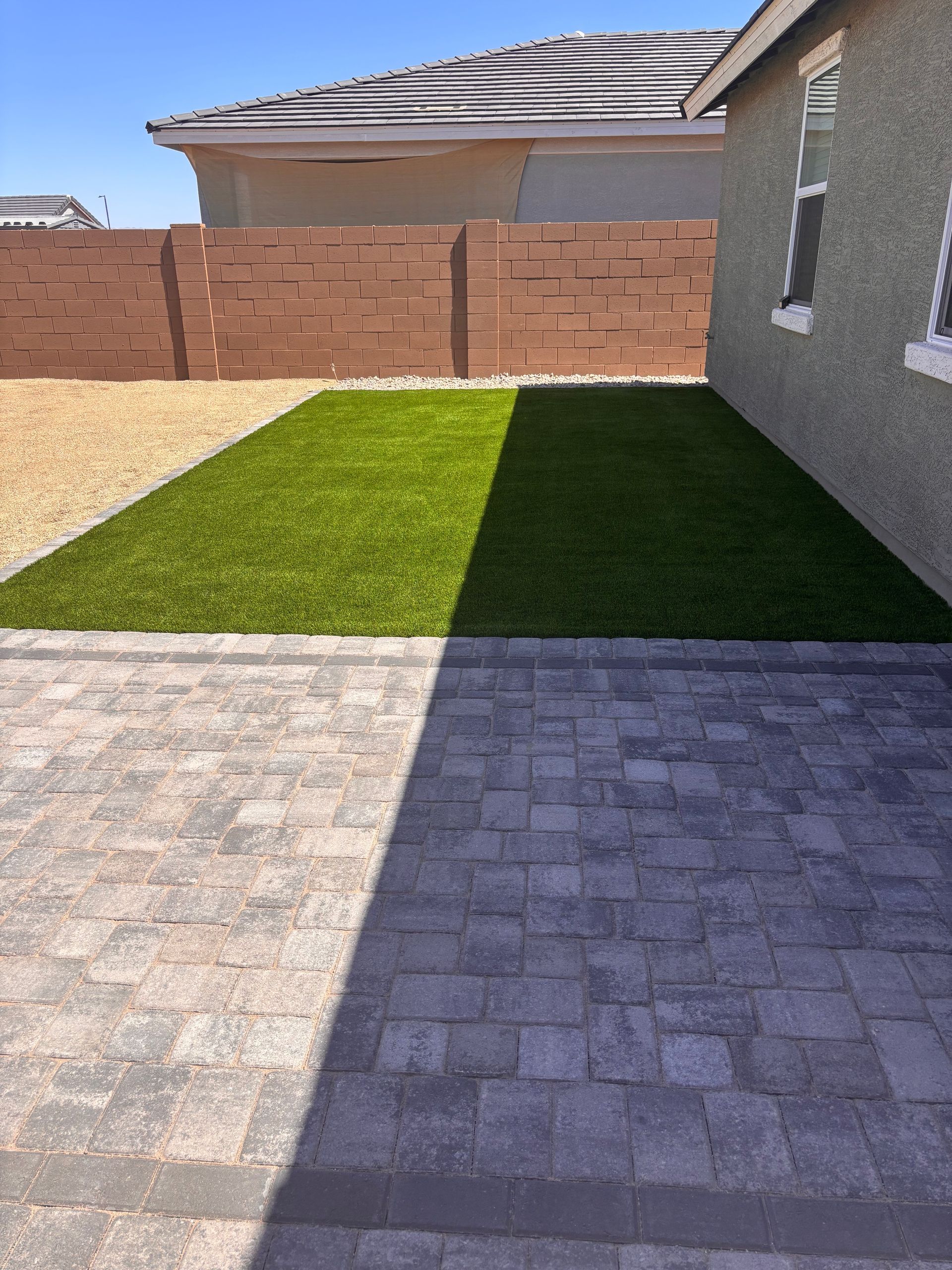 Backyard with a brick patio, artificial turf, and a brown fence on a sunny day.