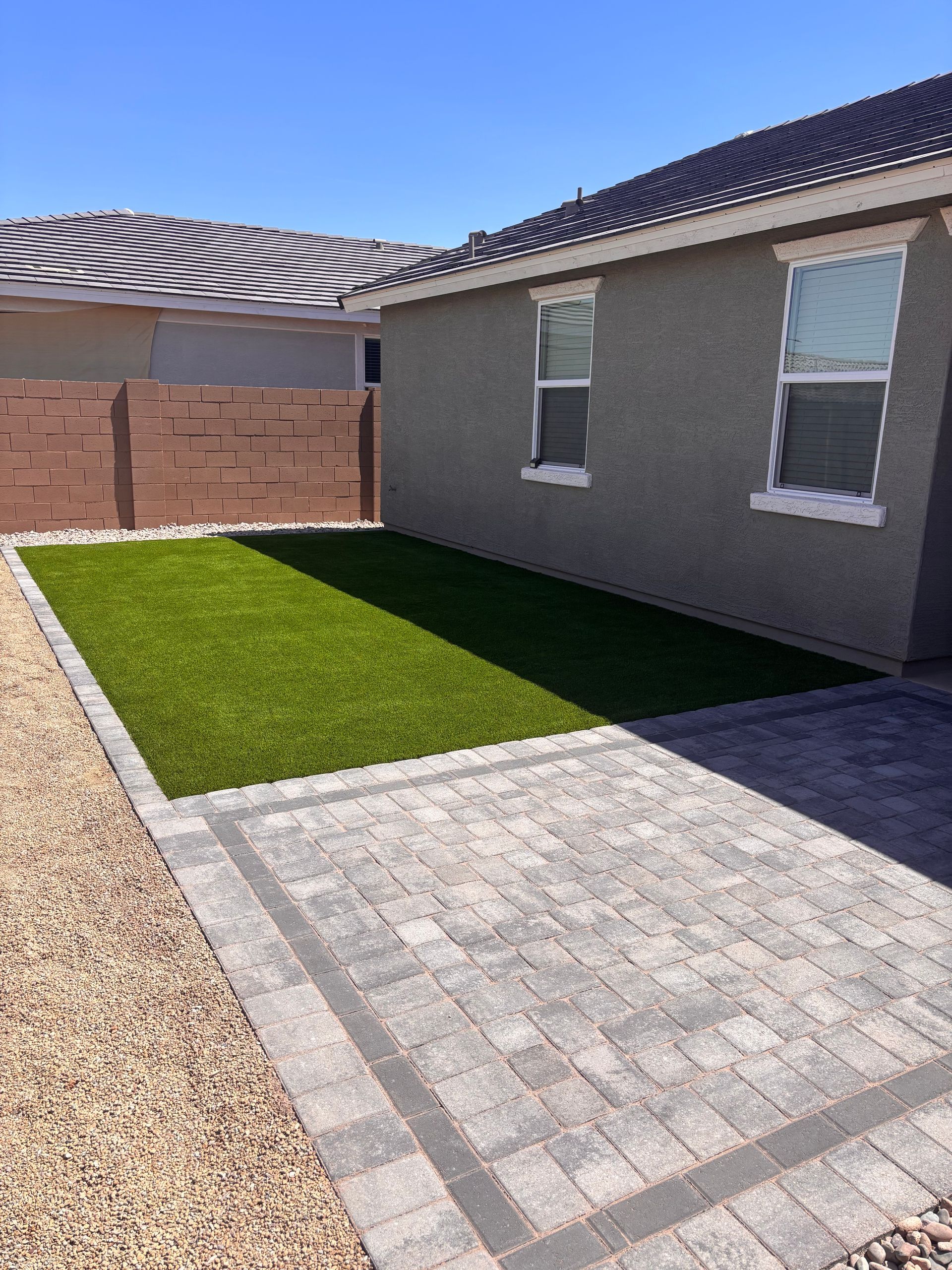 A backyard with a green artificial turf area, paved path, and brown fence.