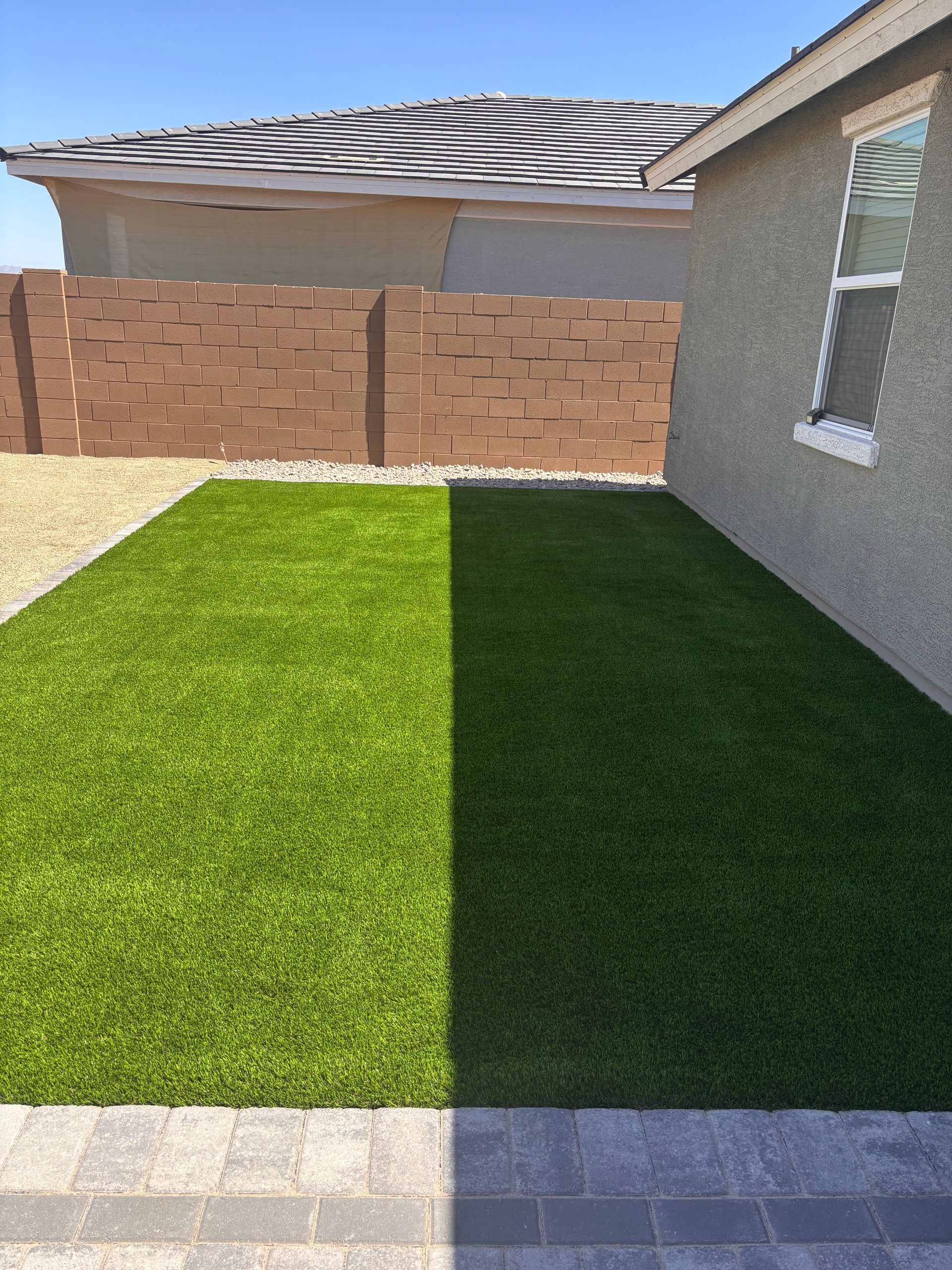 Backyard with artificial turf, brown brick wall, and a light-colored stucco house.