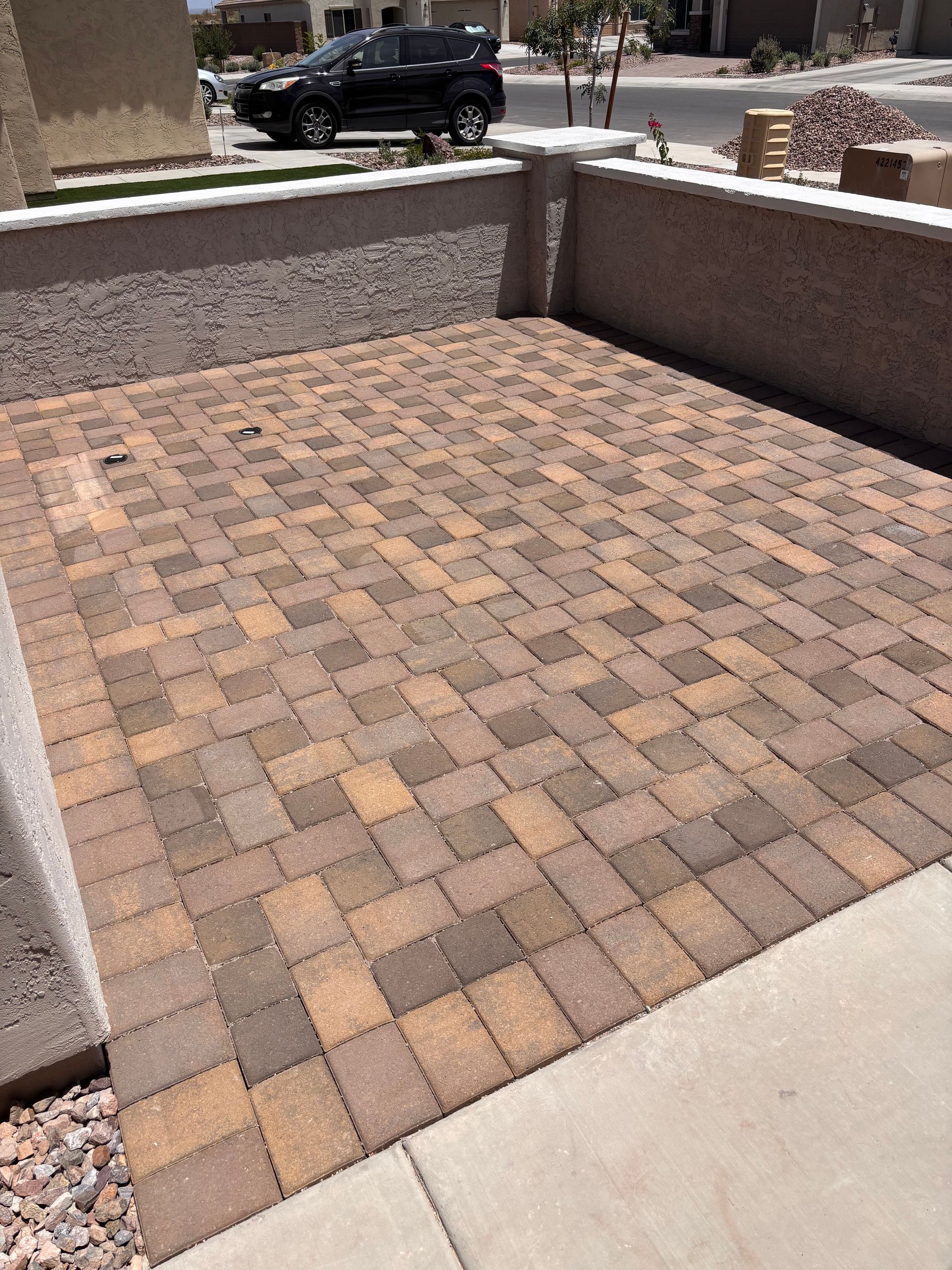 Brick patio enclosed by walls, with a concrete border, in front of a house.