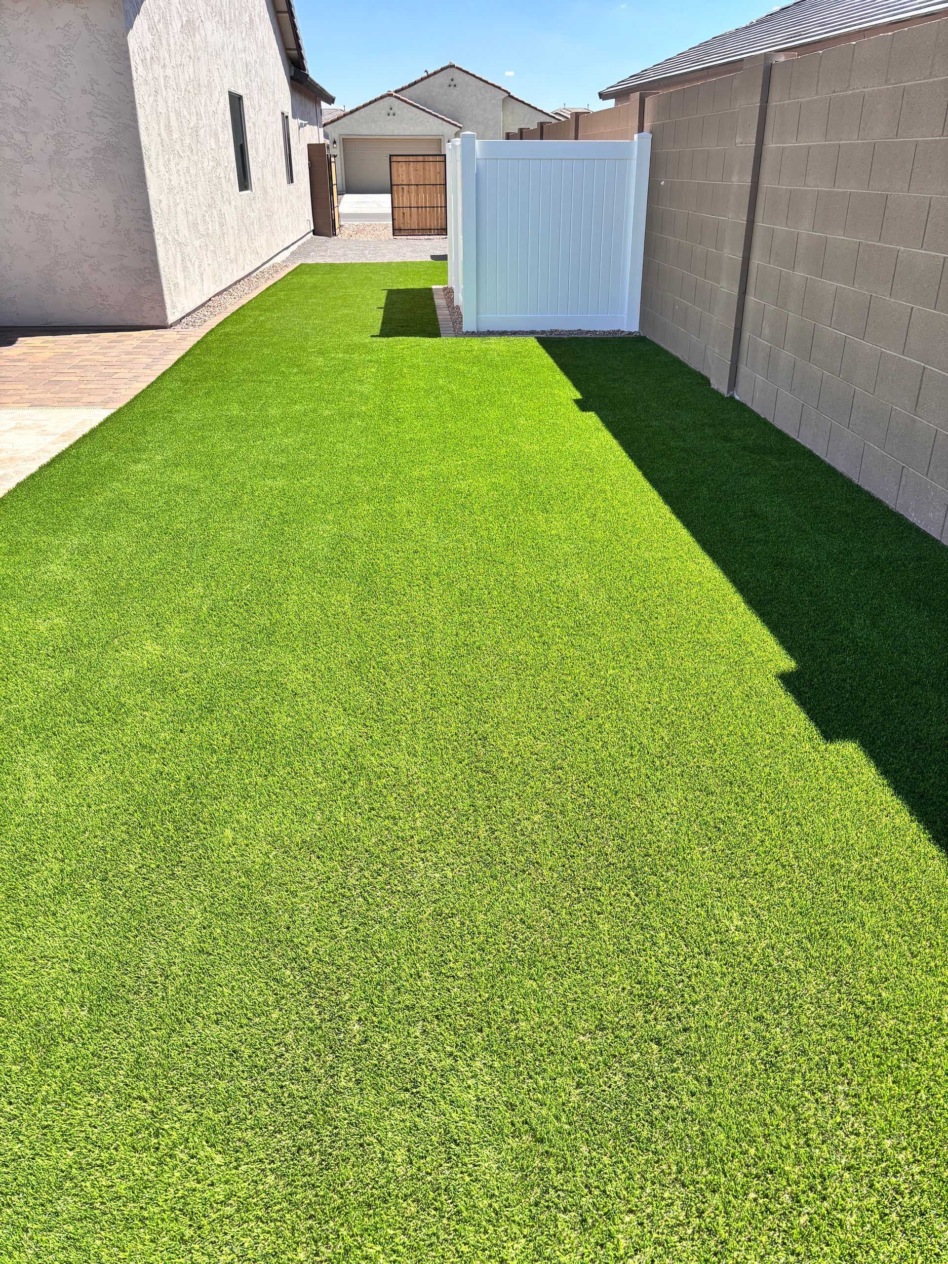 Green artificial grass in a narrow backyard, between white and beige walls.
