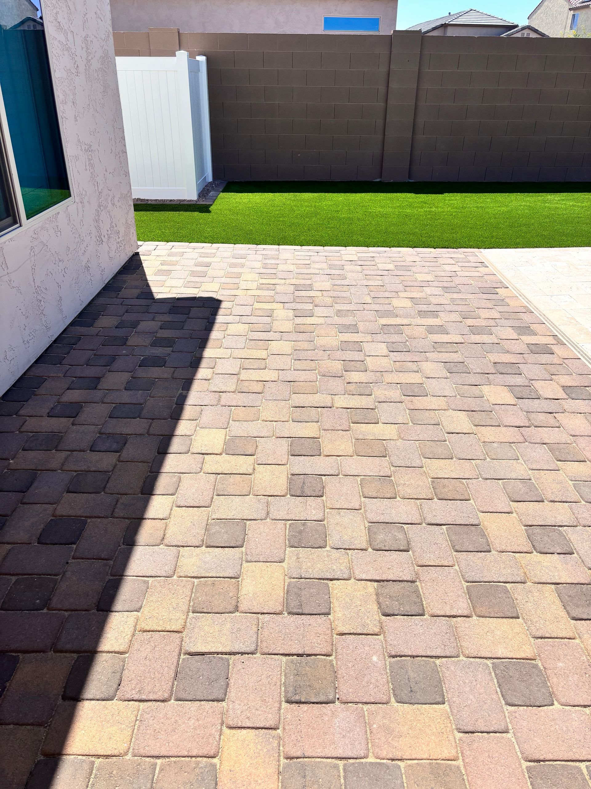 Brick patio with shadow, leading to green turf and a dark fence.