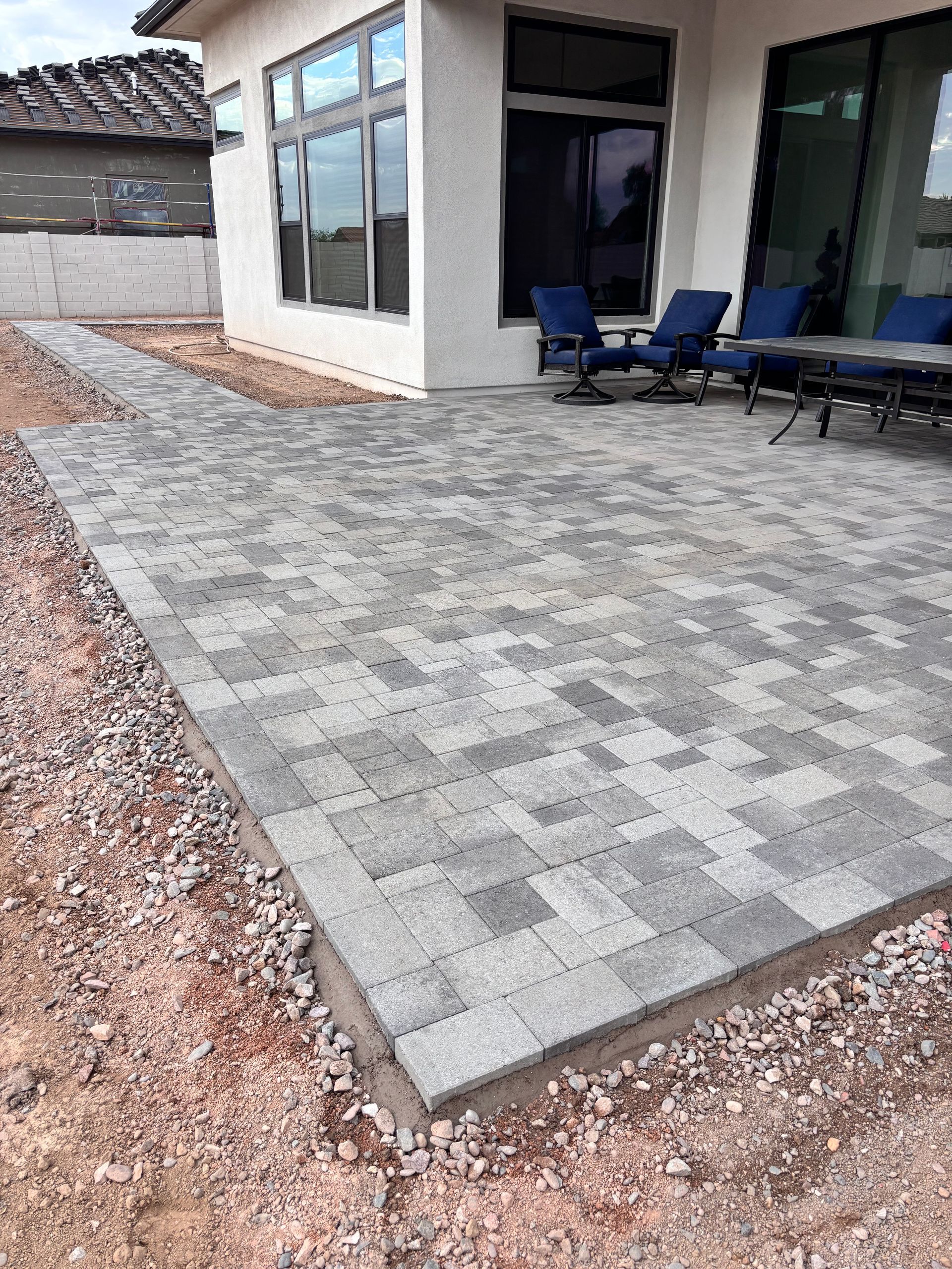 Gray paver patio with matching walkway extending from a white house.  Outdoor seating visible.