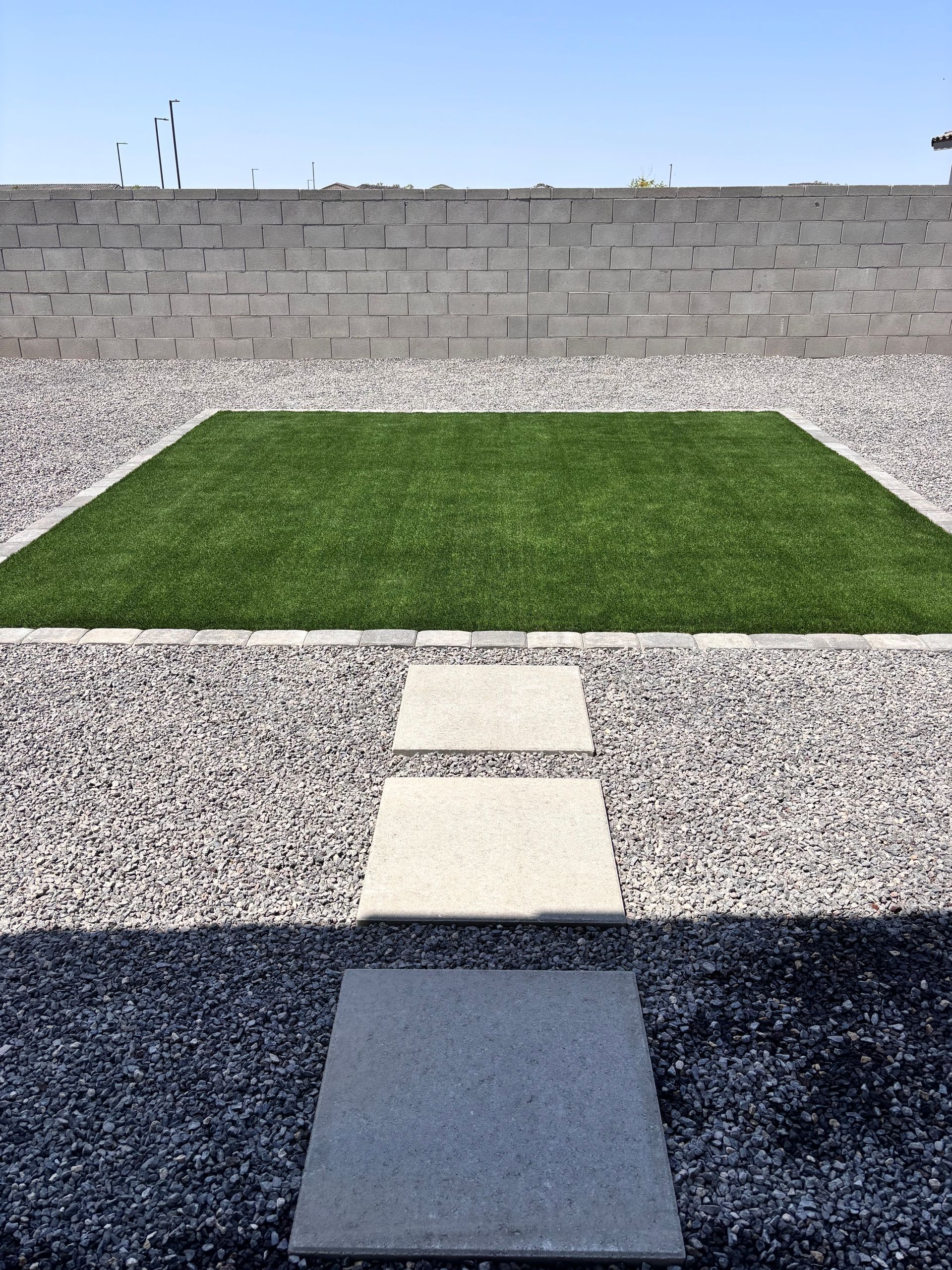 Square of green grass framed by gravel, with stone stepping stones leading toward it.