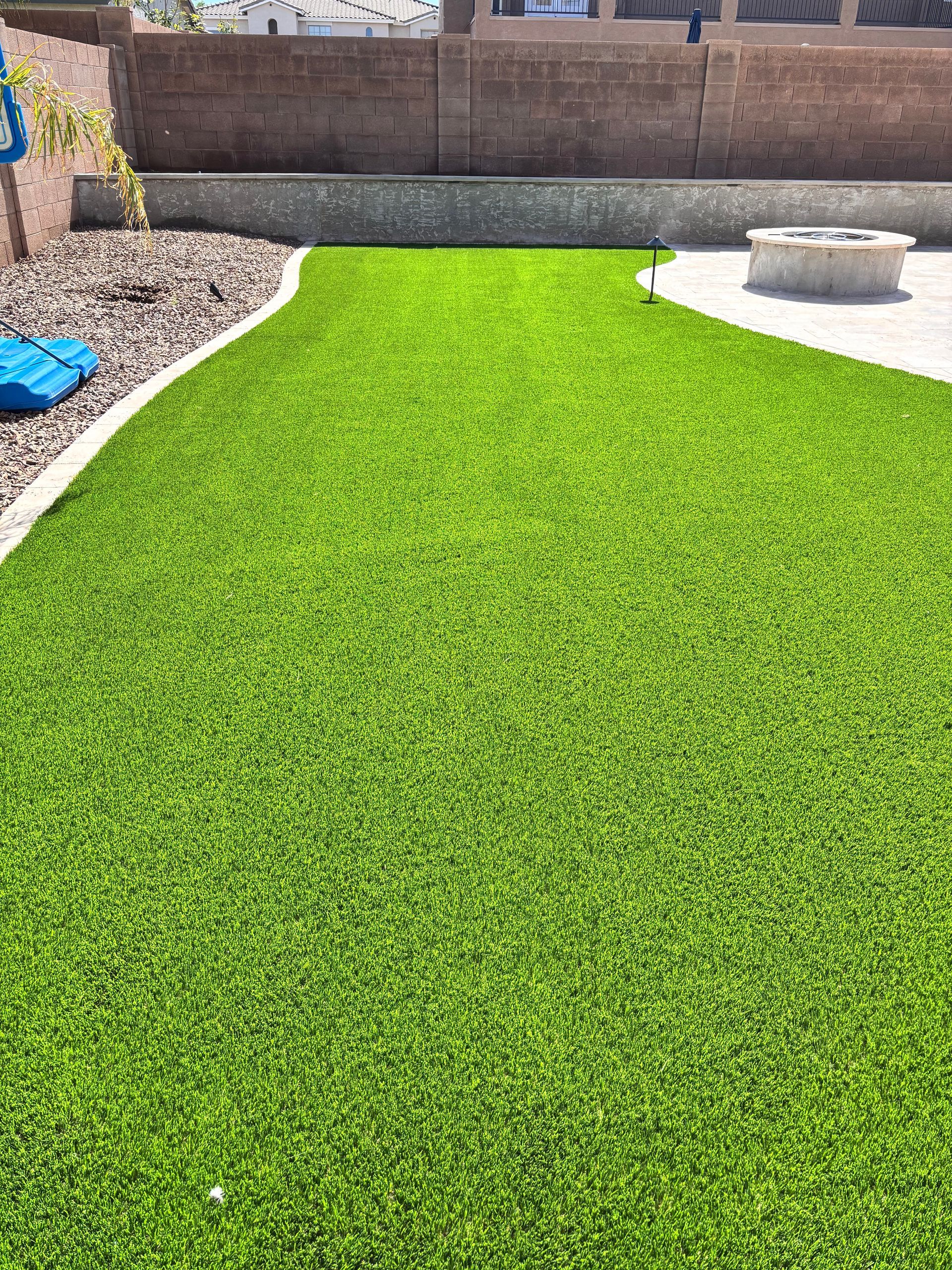 Lush green artificial turf in a backyard with a fire pit and a low wall.