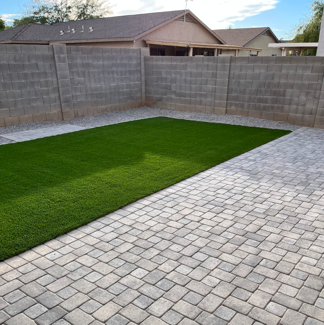 A brick patio with a large patch of grass in the middle