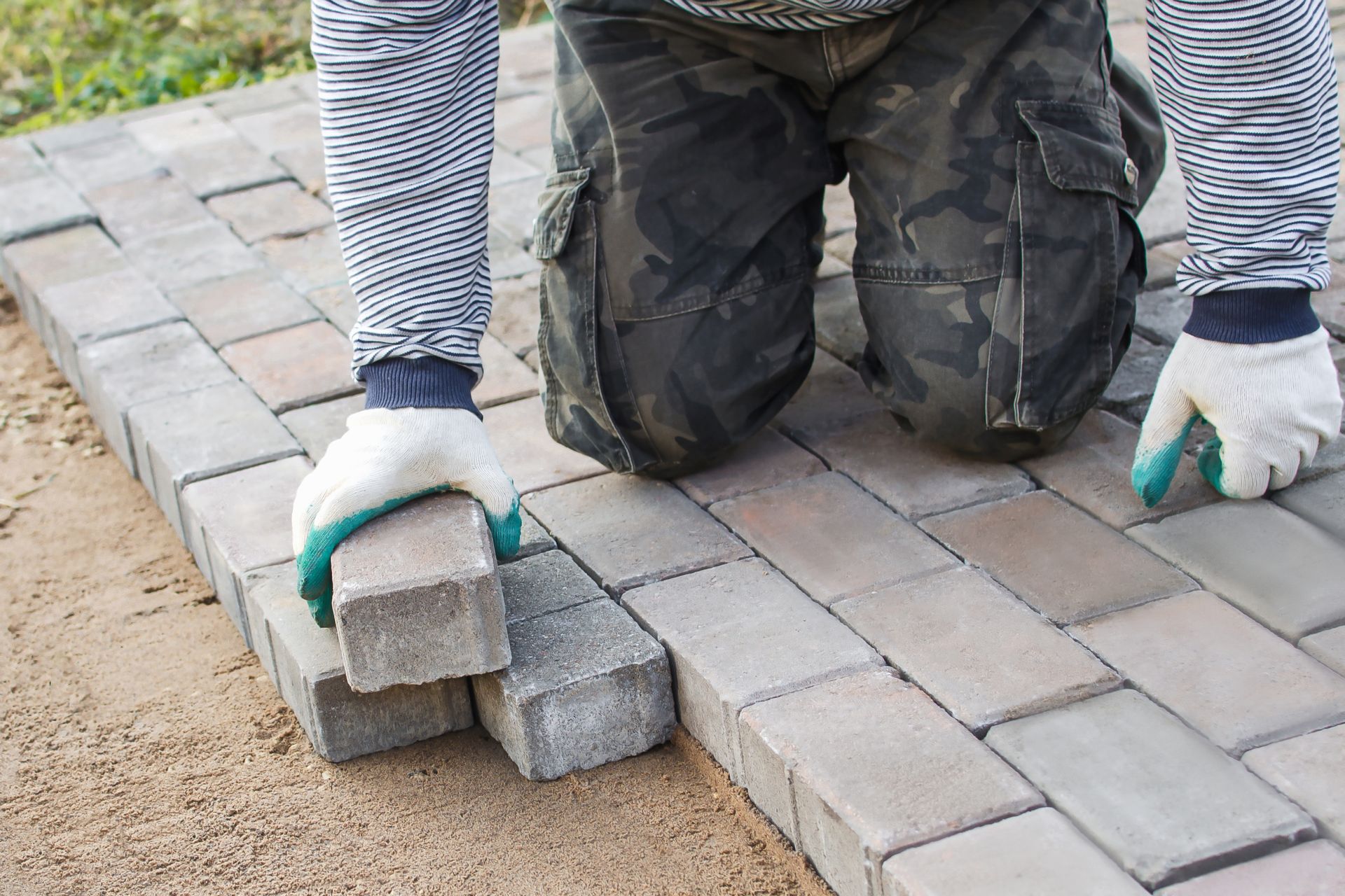 A person is laying bricks on a sidewalk.