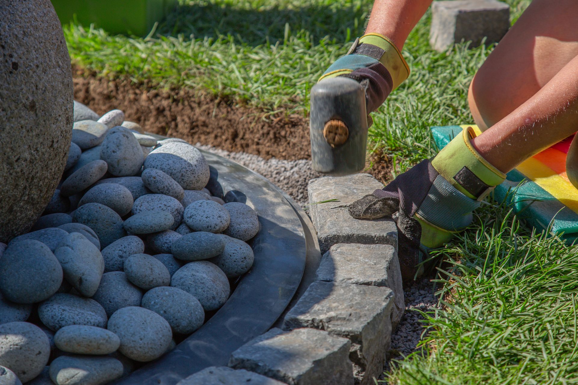 A person is laying bricks in a garden with a hammer.