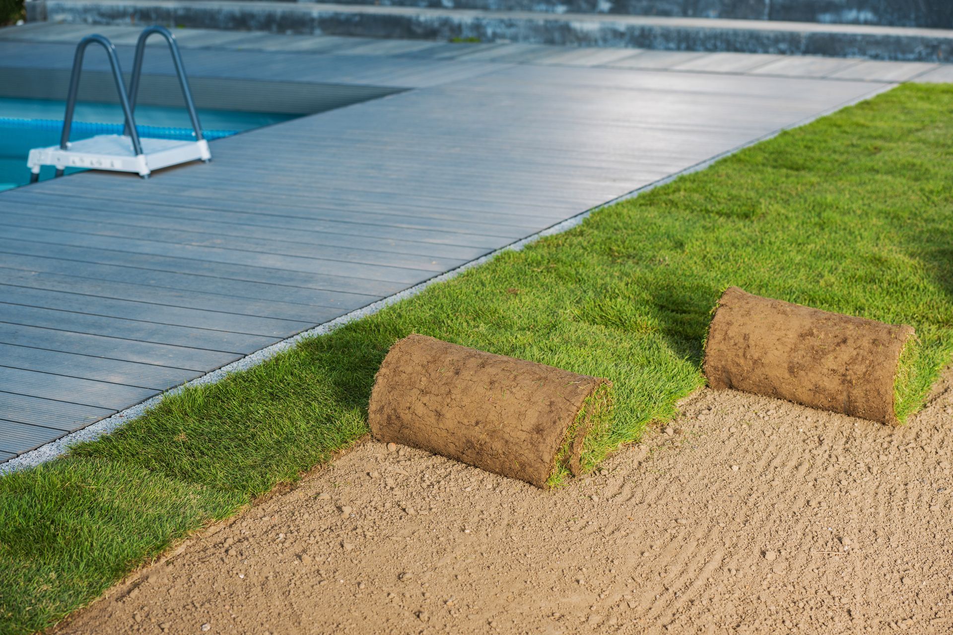 Two rolls of turf are sitting next to a swimming pool.
