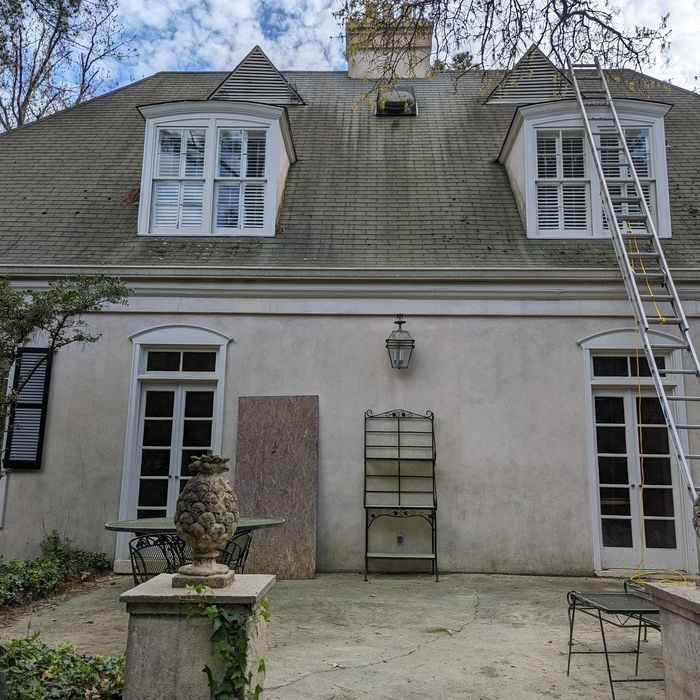 A two-story building with dormer windows, a ladder, and outdoor furniture. The sky is cloudy.