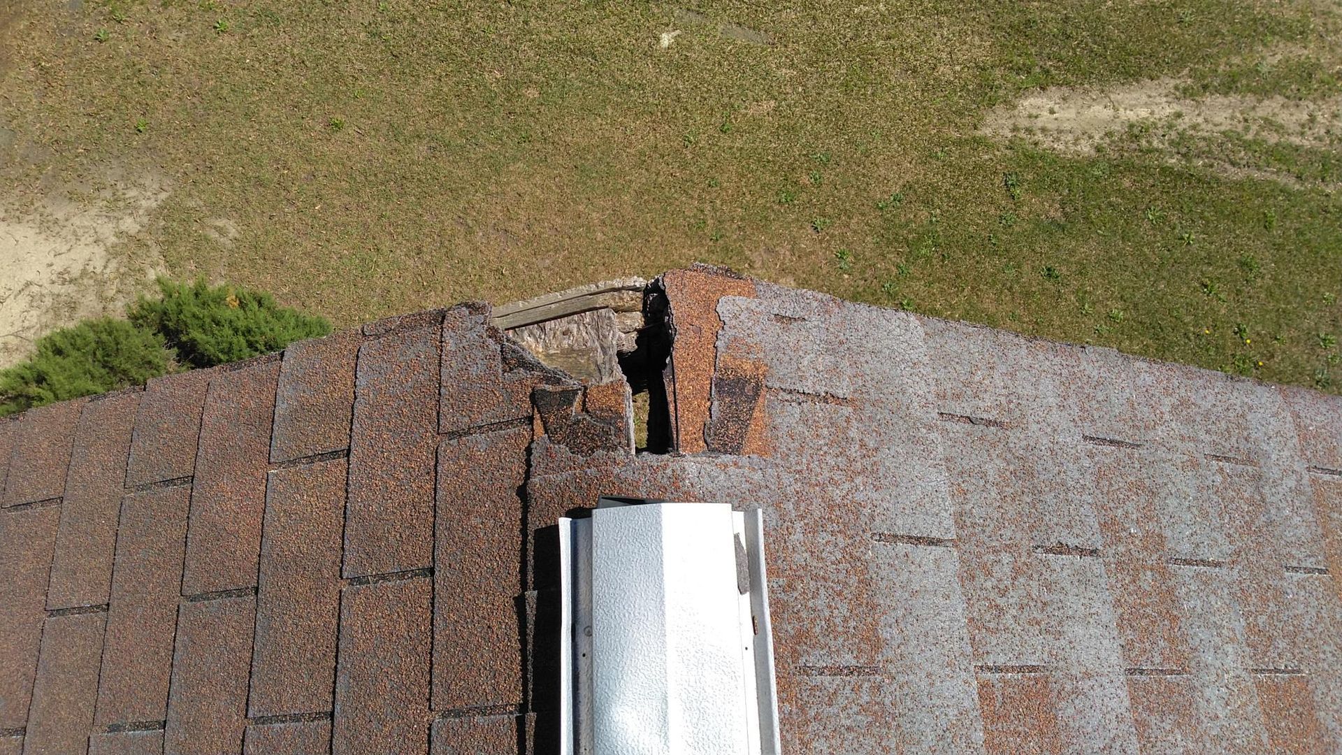 Damaged roof shingles around a metal vent pipe with missing pieces exposing the underlayment