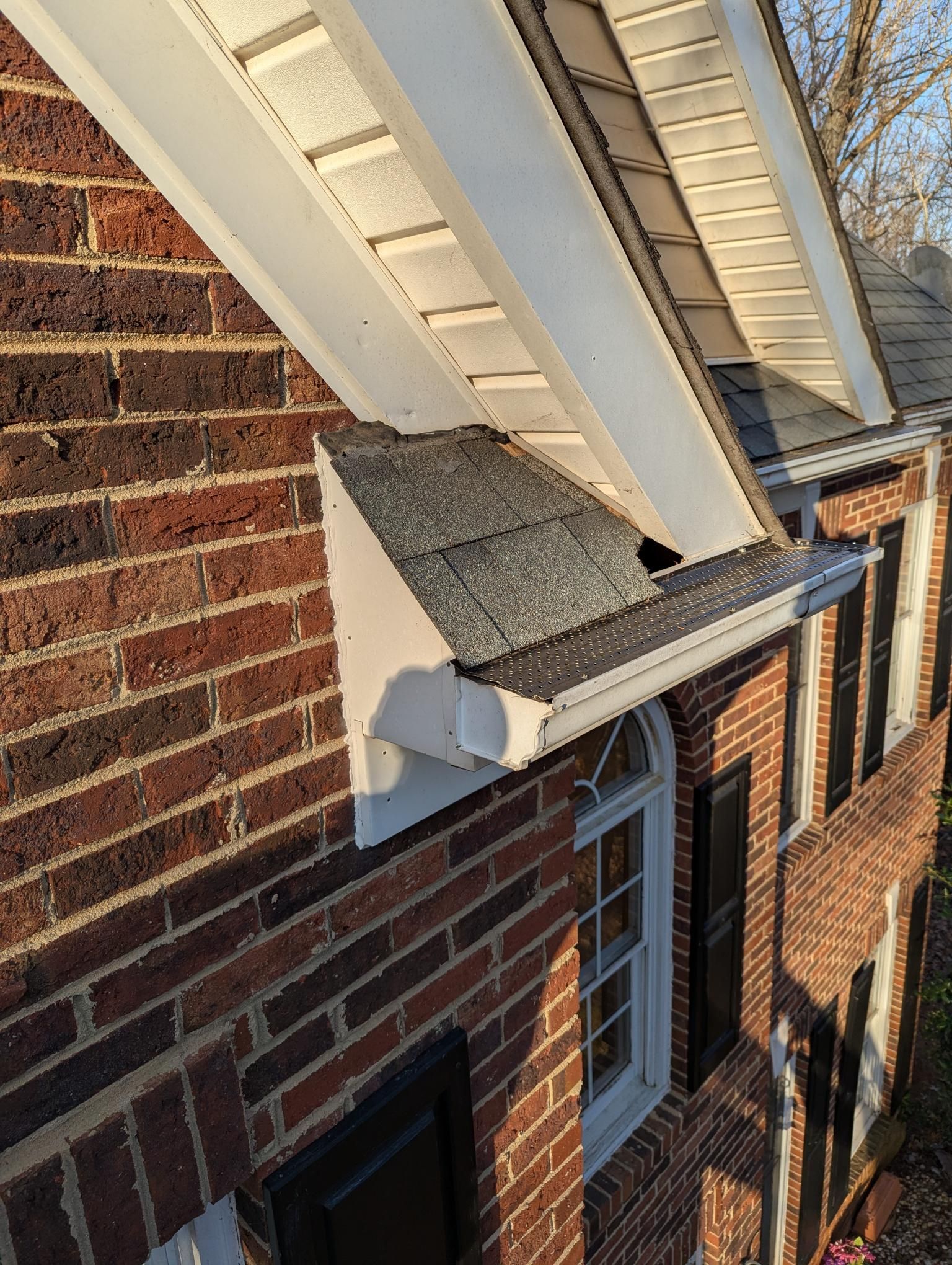 Brick house with white dormer roof and window above a sloped roof in bright daylight