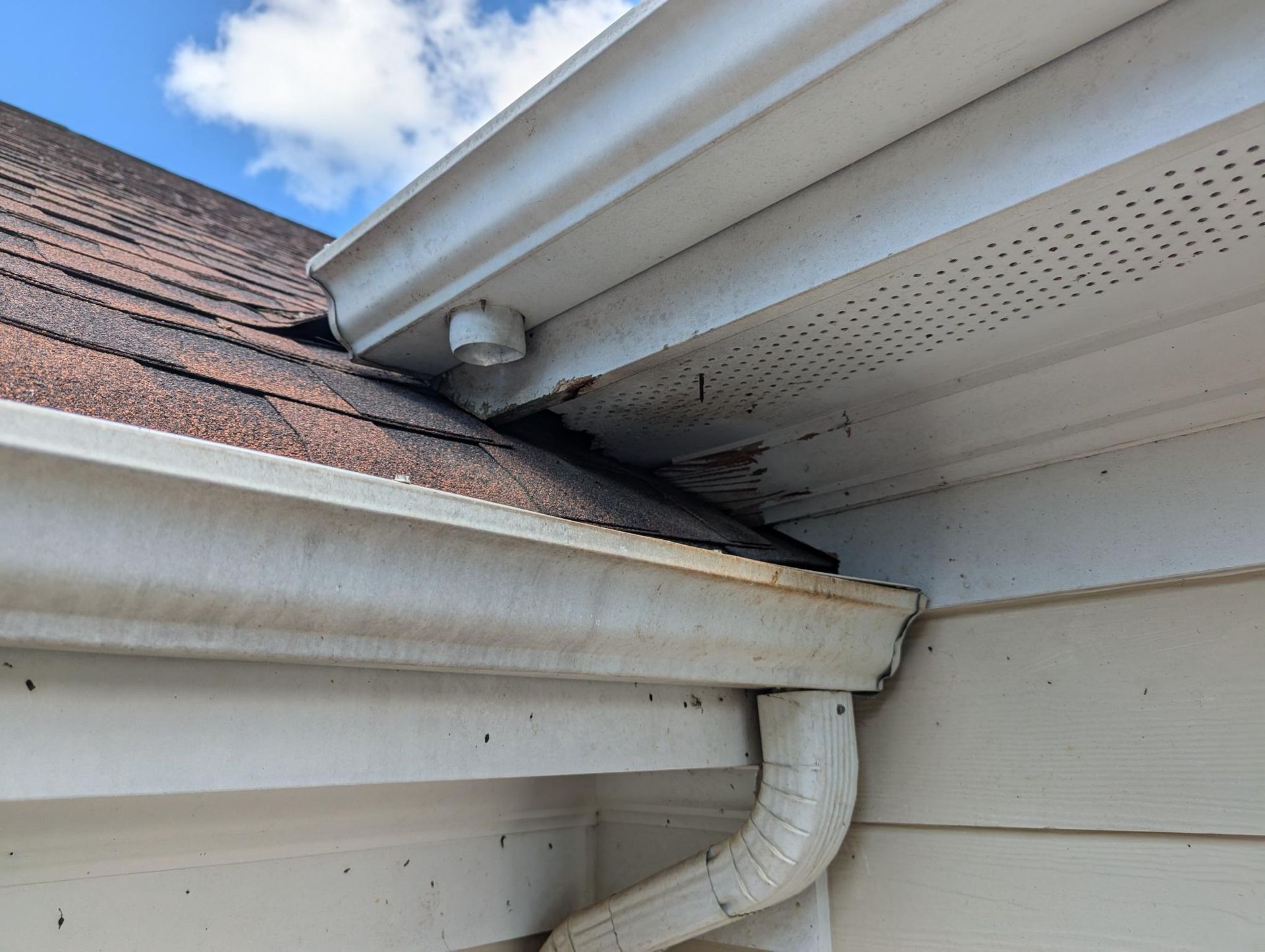 Close-up of a roof gutter and downspout with a visible gap where water could leak under the eaves