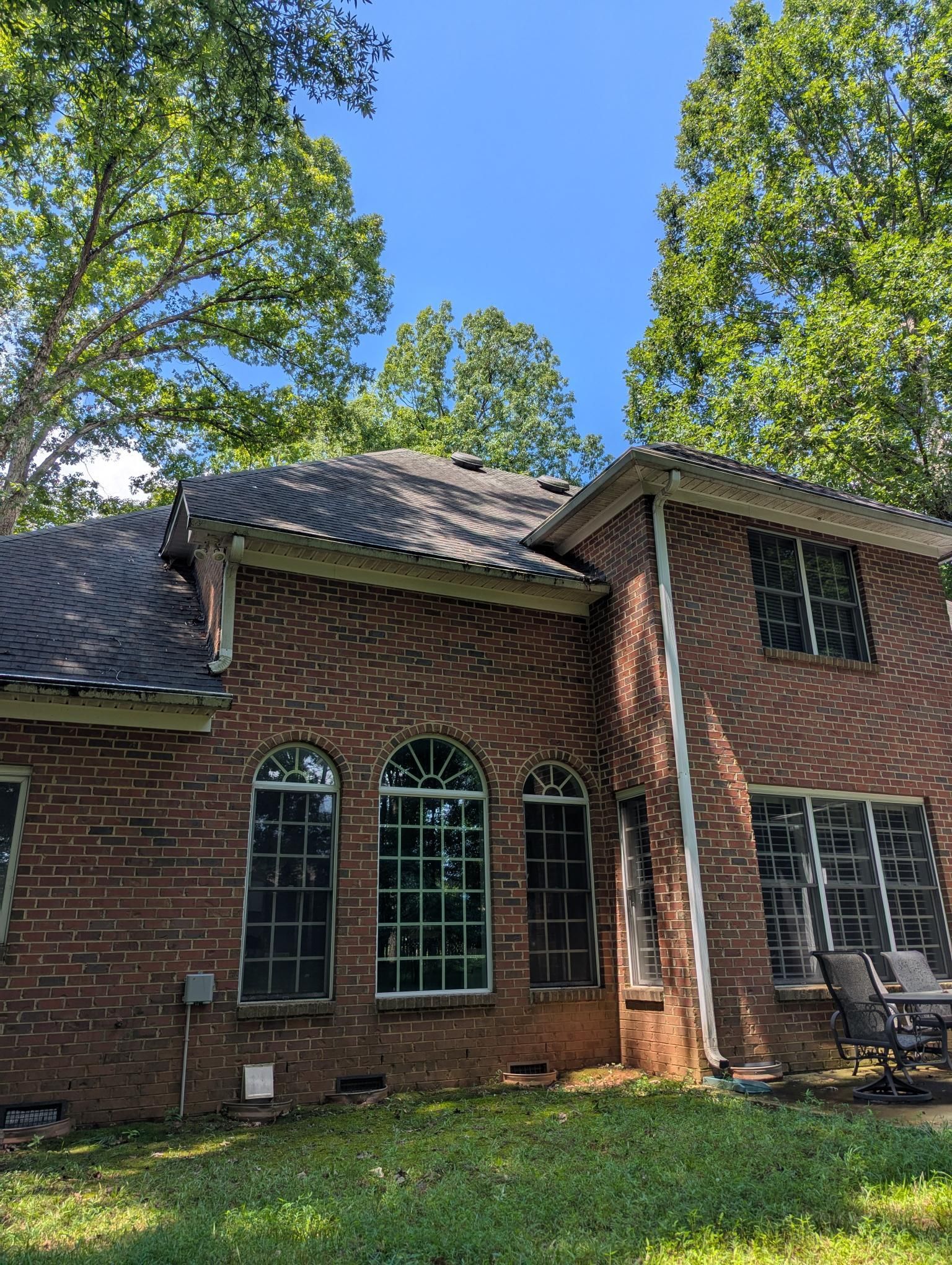 Brick house exterior with arched windows, a sloped roof, and tall trees in the yard