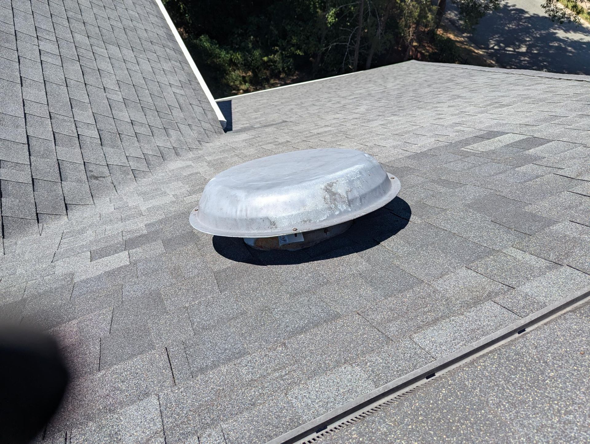 A rooftop vent covered with white protective plastic on a gray shingled roof.