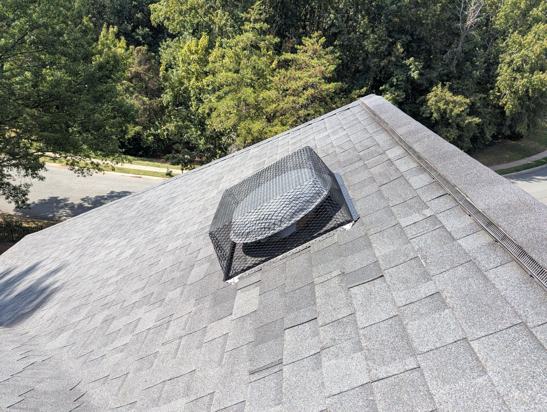 Roof vent on gray shingle roof with trees in the background