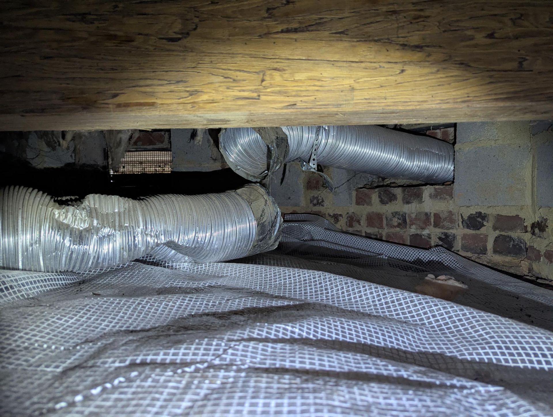 Insulated HVAC ducts and pipes in a crawlspace beneath wooden floor joists