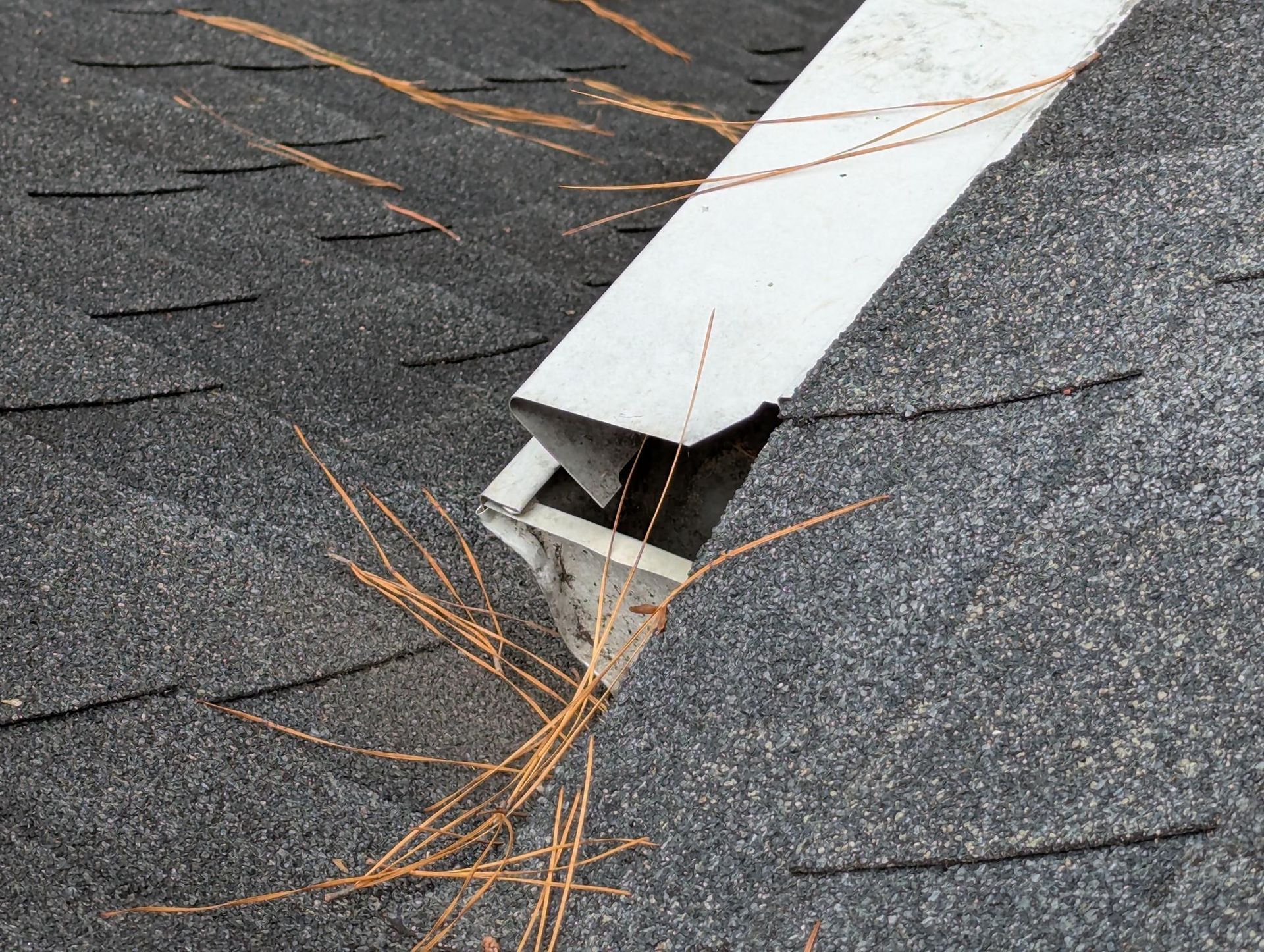 Damaged metal roof vent with orange debris on gray shingles