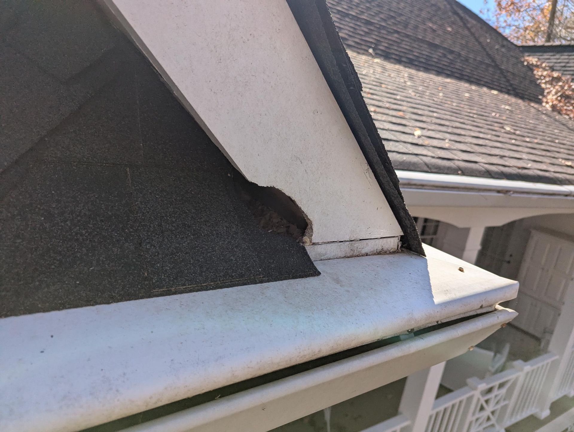 Close-up of a damaged roof corner with torn shingles and a bent white fascia board.