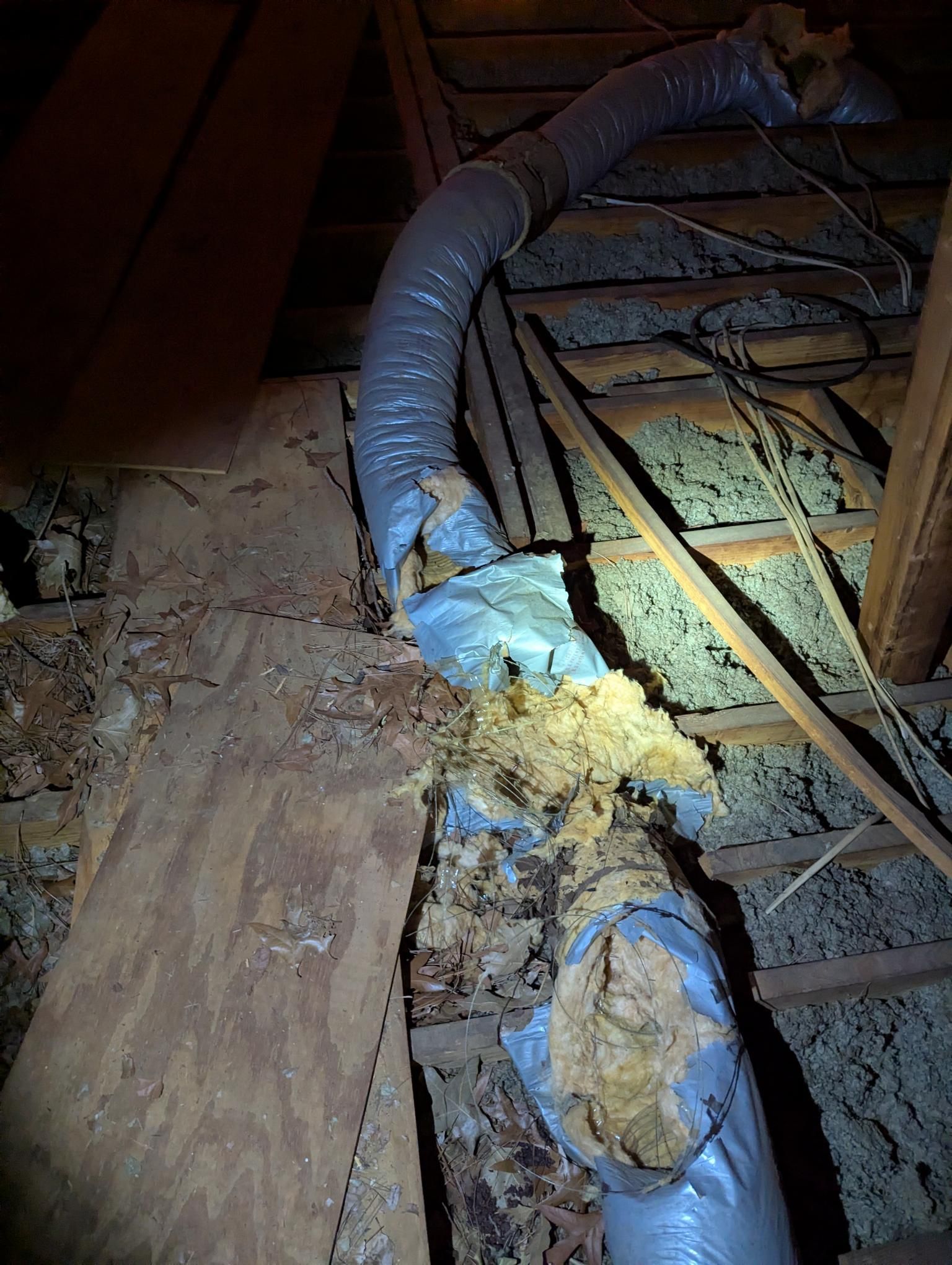 Damaged attic insulation and ductwork with exposed wood beams and debris on the floor