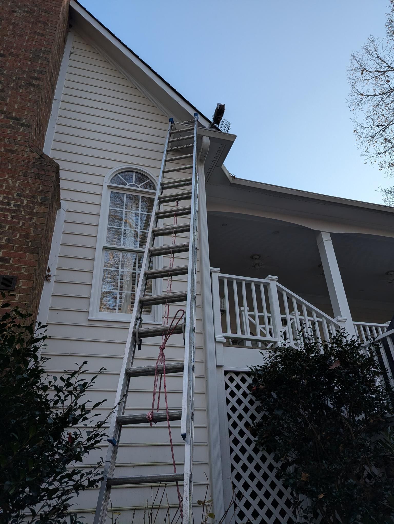 Ladder leaning against a house beside a porch, reaching up to the roofline.
