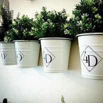 White planters with green plants on a white wall, each with a logo.