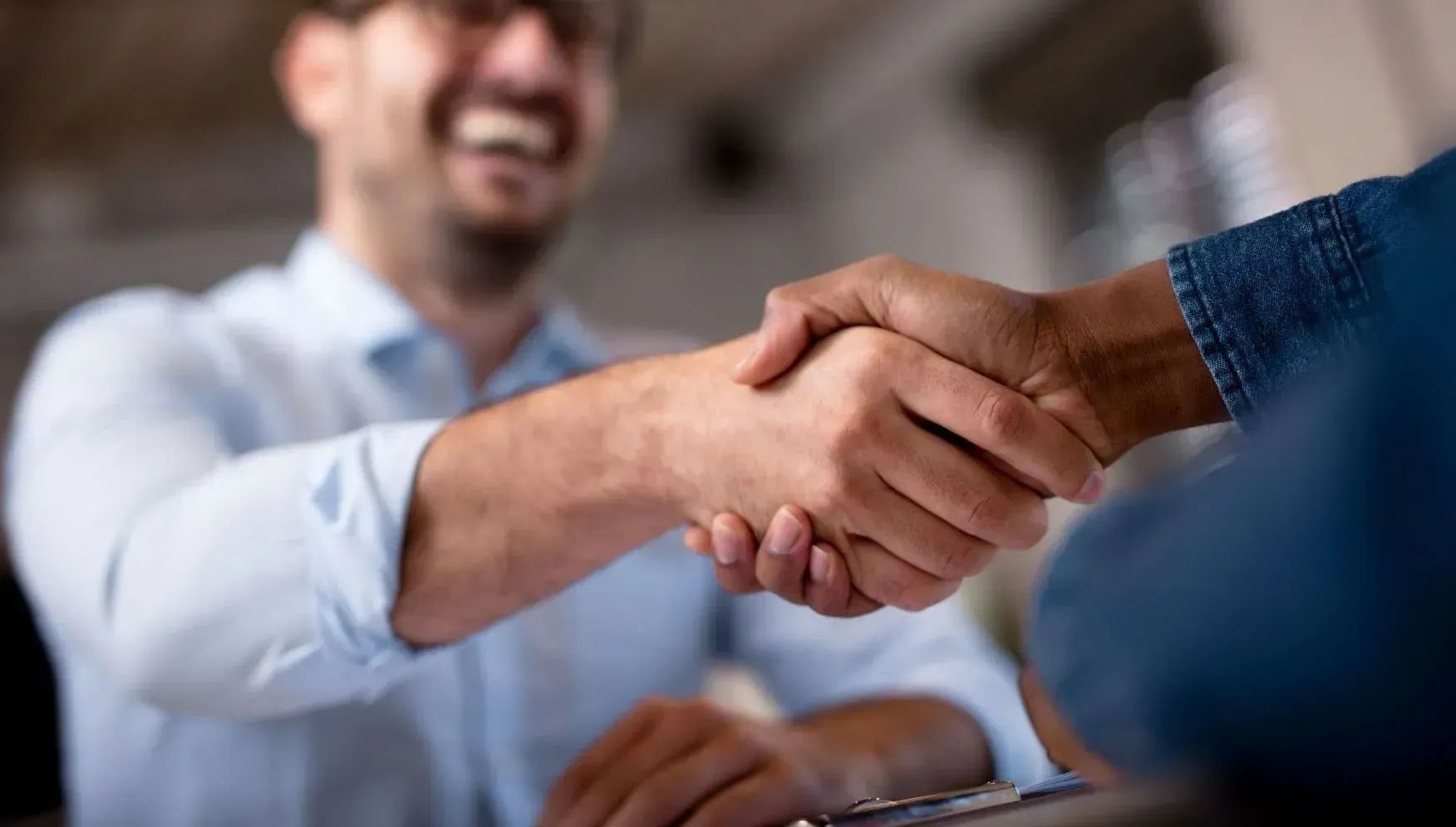 Two people shaking hands in an office, with one person blurred in the background.
