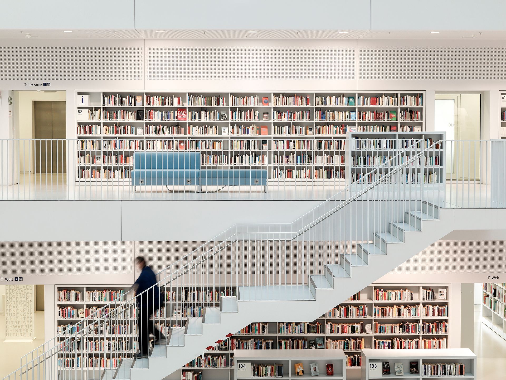 Bibliothek mit weißen Bücherregalen, einer Treppe und einer Person.Fotograf Tübingen. Fotograf Reutlingen.
