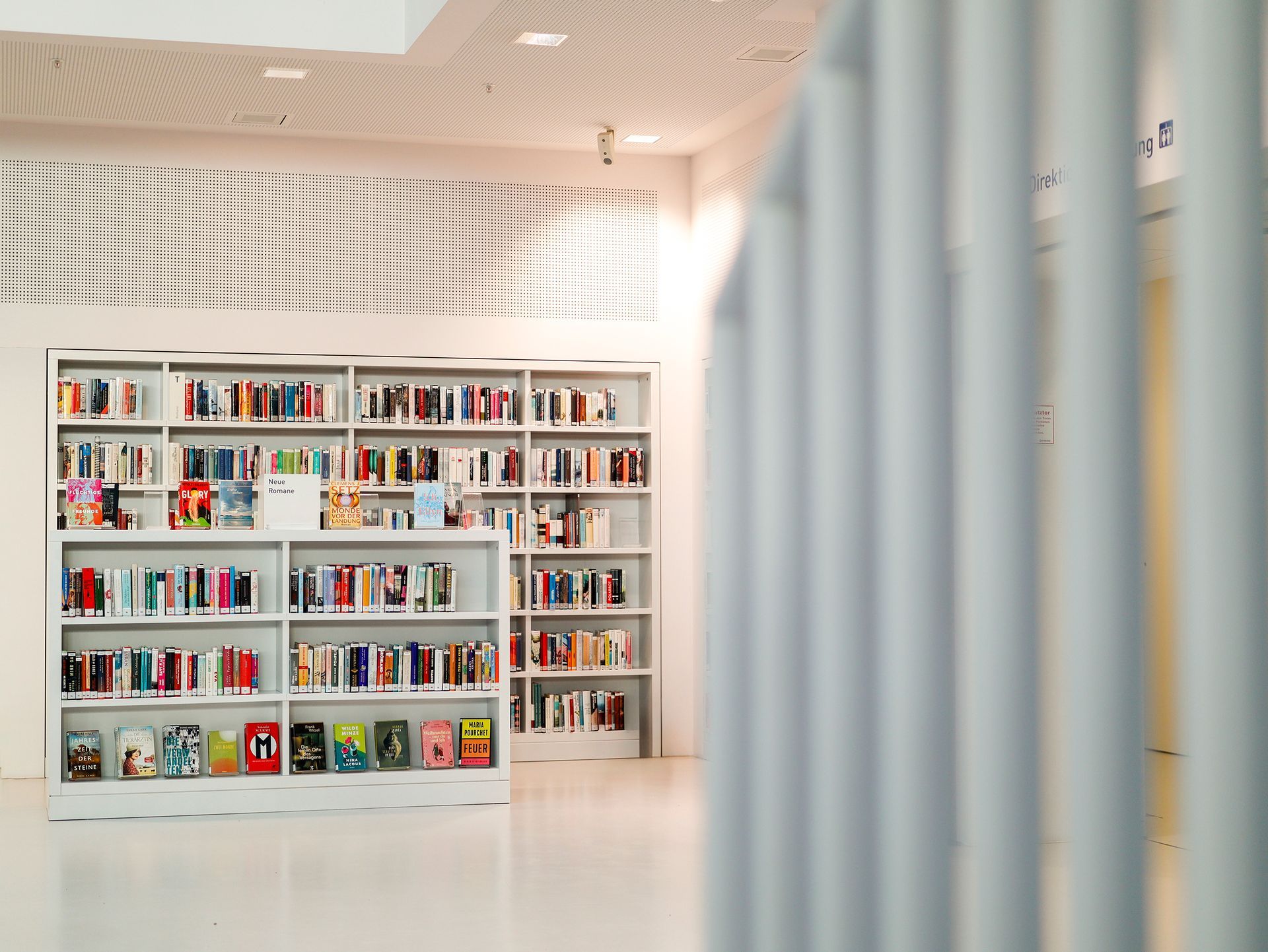 Weiße Bücherregale voller Bücher in einer Bibliothek, hinter weißen vertikalen Balken.Fotograf Tübingen. Fotograf Reutlingen.