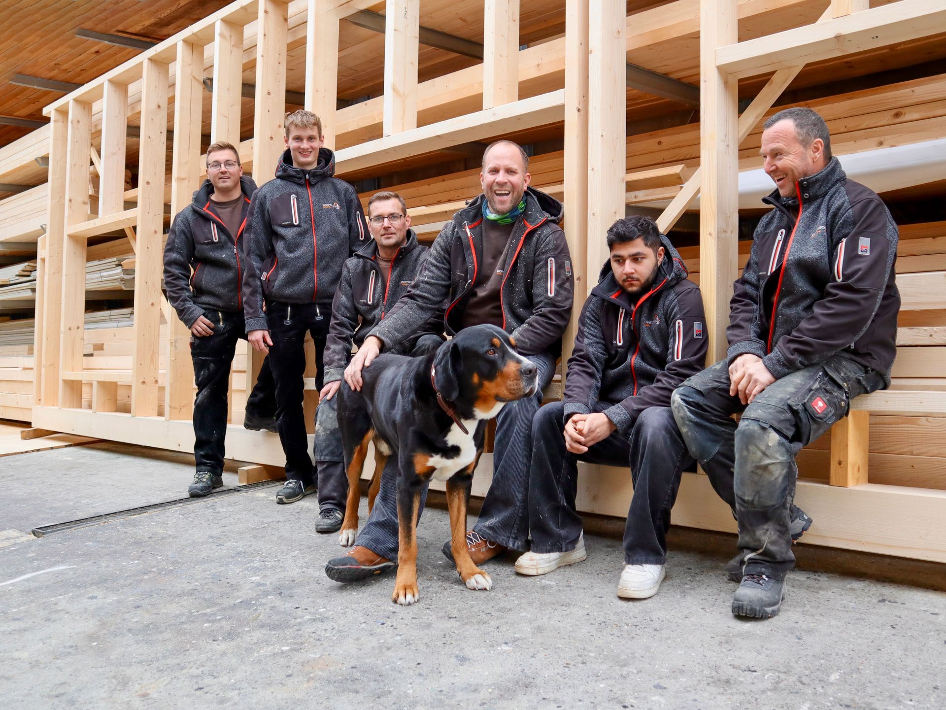 Zimmermänner mit Hund posieren vor Holz, alle tragen die gleichen Jacken.Fotograf Tübingen. Fotograf Reutlingen.