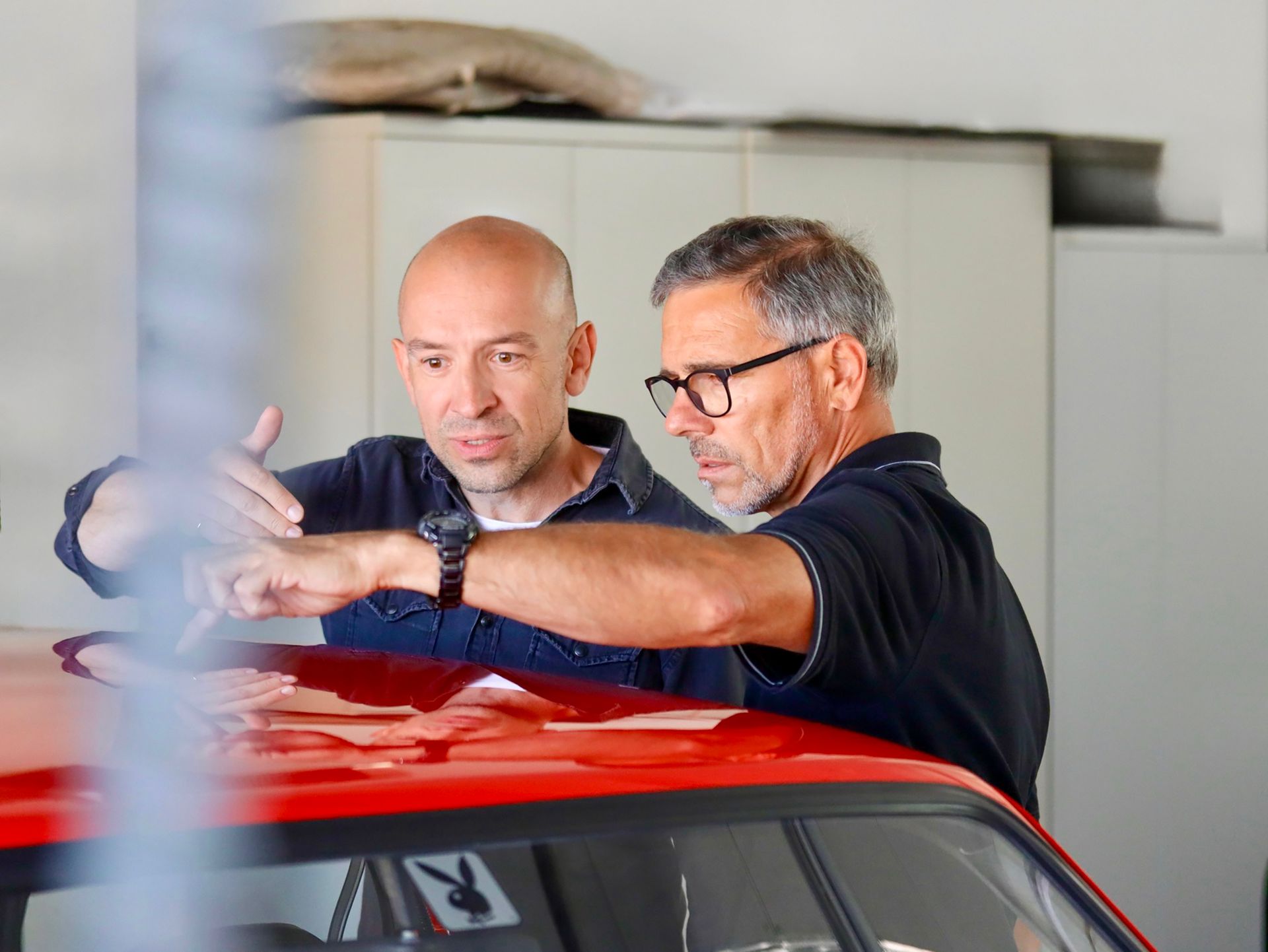 Zwei Männer untersuchen in einer Garage das Dach eines roten Autos. Fotograf Tübingen. Fotograf Reutlingen.