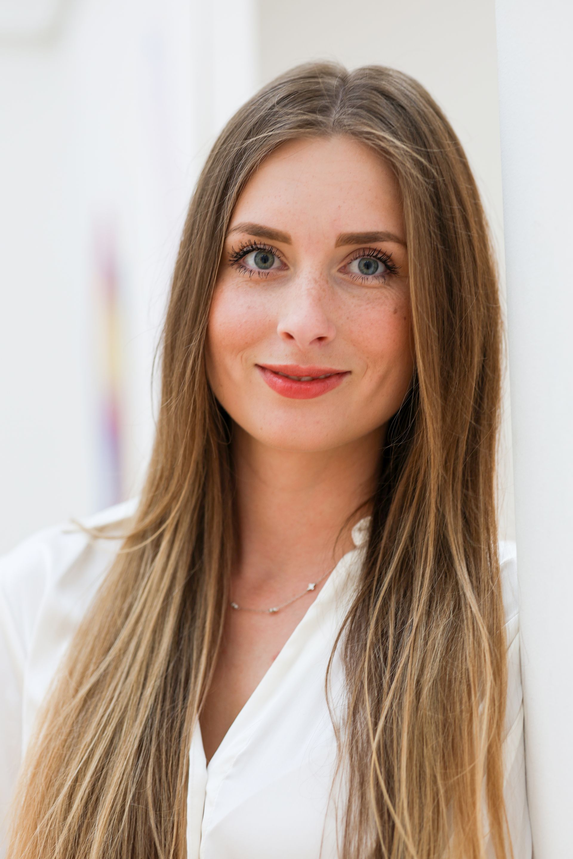 Eine Frau mit langen blonden Haaren lächelt sanft und lehnt an einer weißen Wand.Fotograf Tübingen. Fotograf Reutlingen.