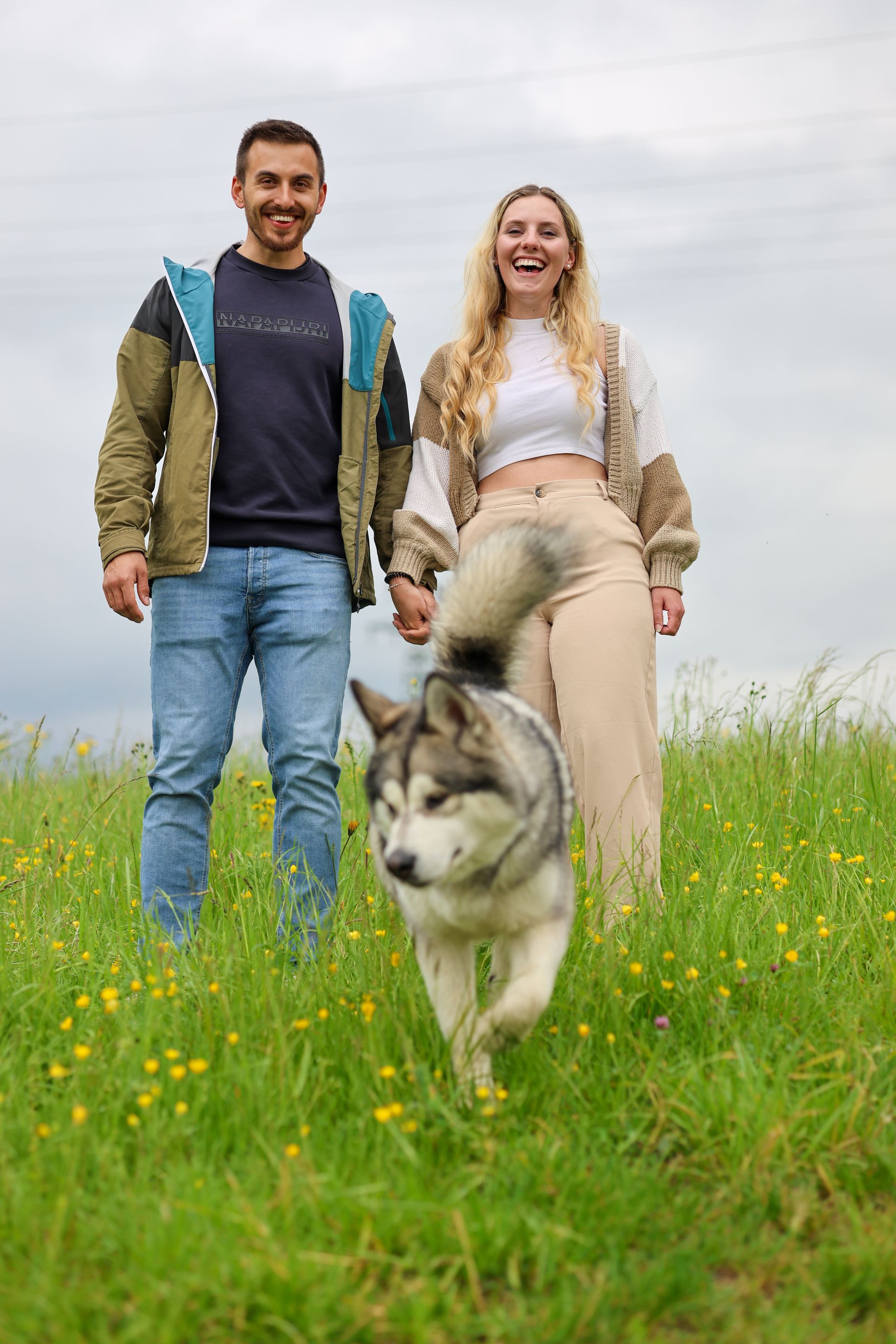 Ein Paar hält Händchen auf einer Wiese, während ein Hund auf sie zuläuft.Fotograf Tübingen. Fotograf Reutlingen.
