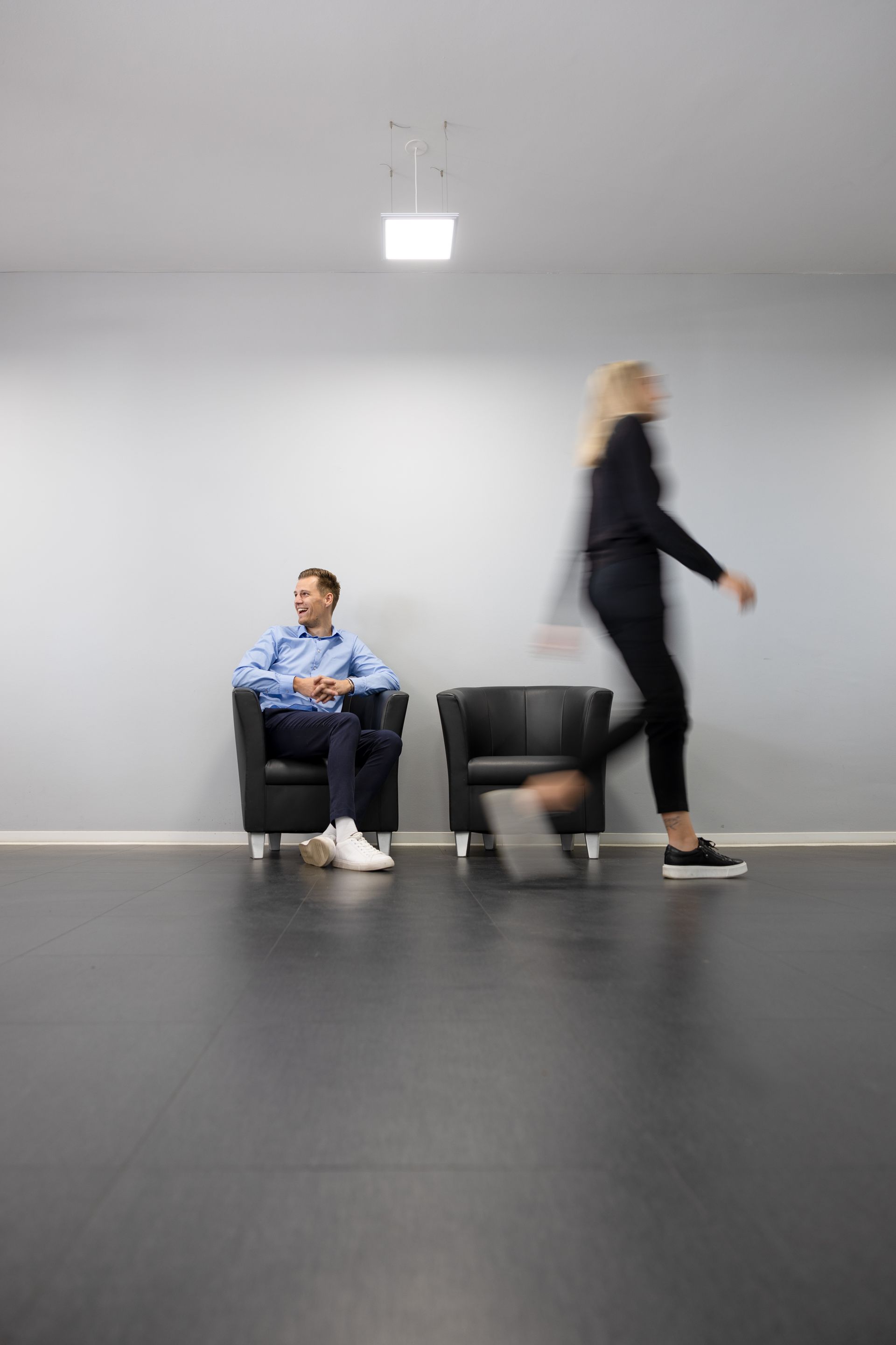 Ein Mann sitzt, eine Frau geht vorbei, in minimalistisch  Raum mit dunklem Boden. Fotograf Tübingen. Fotograf Reutlingen.