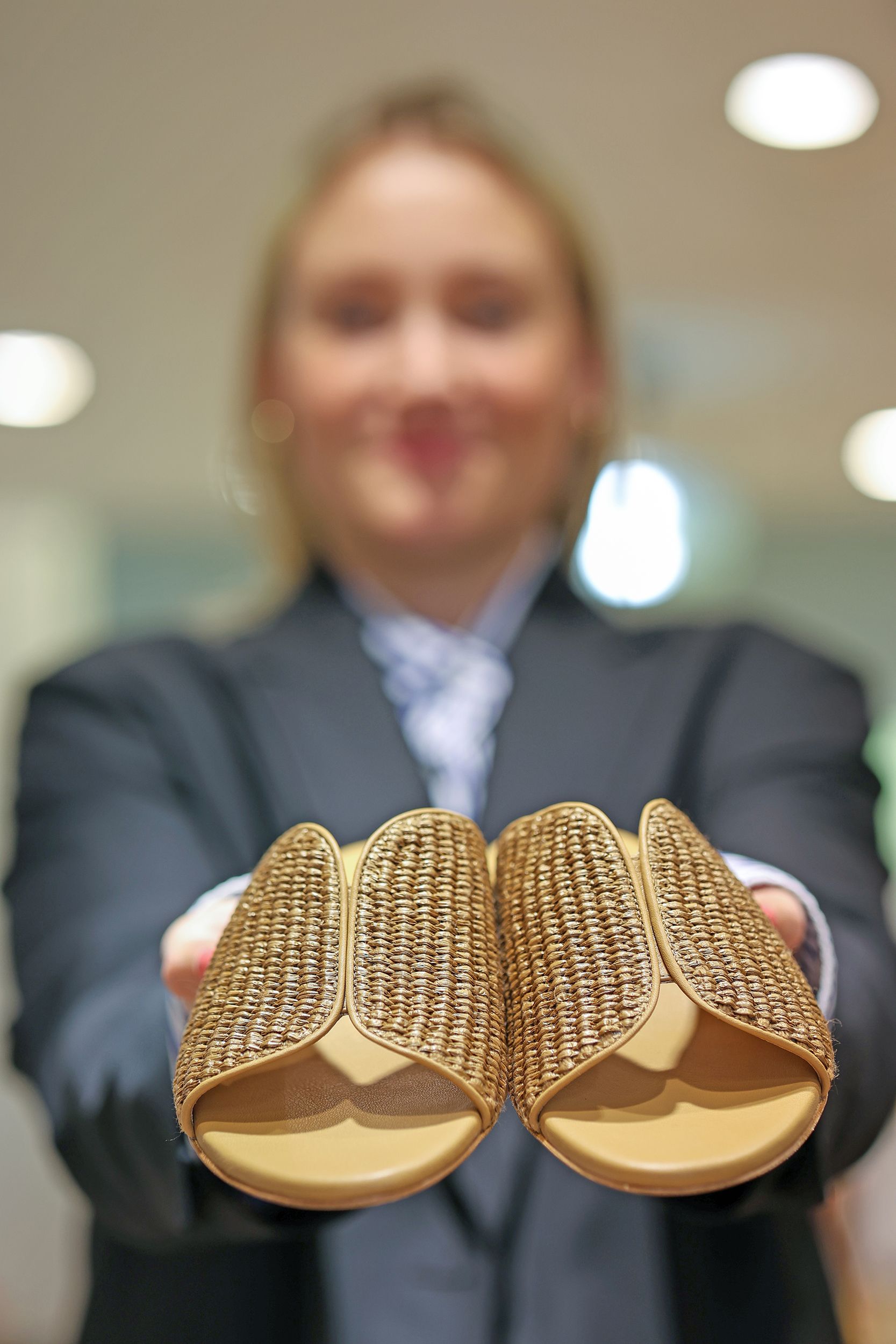 Eine Frau im Anzug hält ein Paar goldfarbene Sandalen hoch.Fotograf Tübingen. Fotograf Reutlingen.