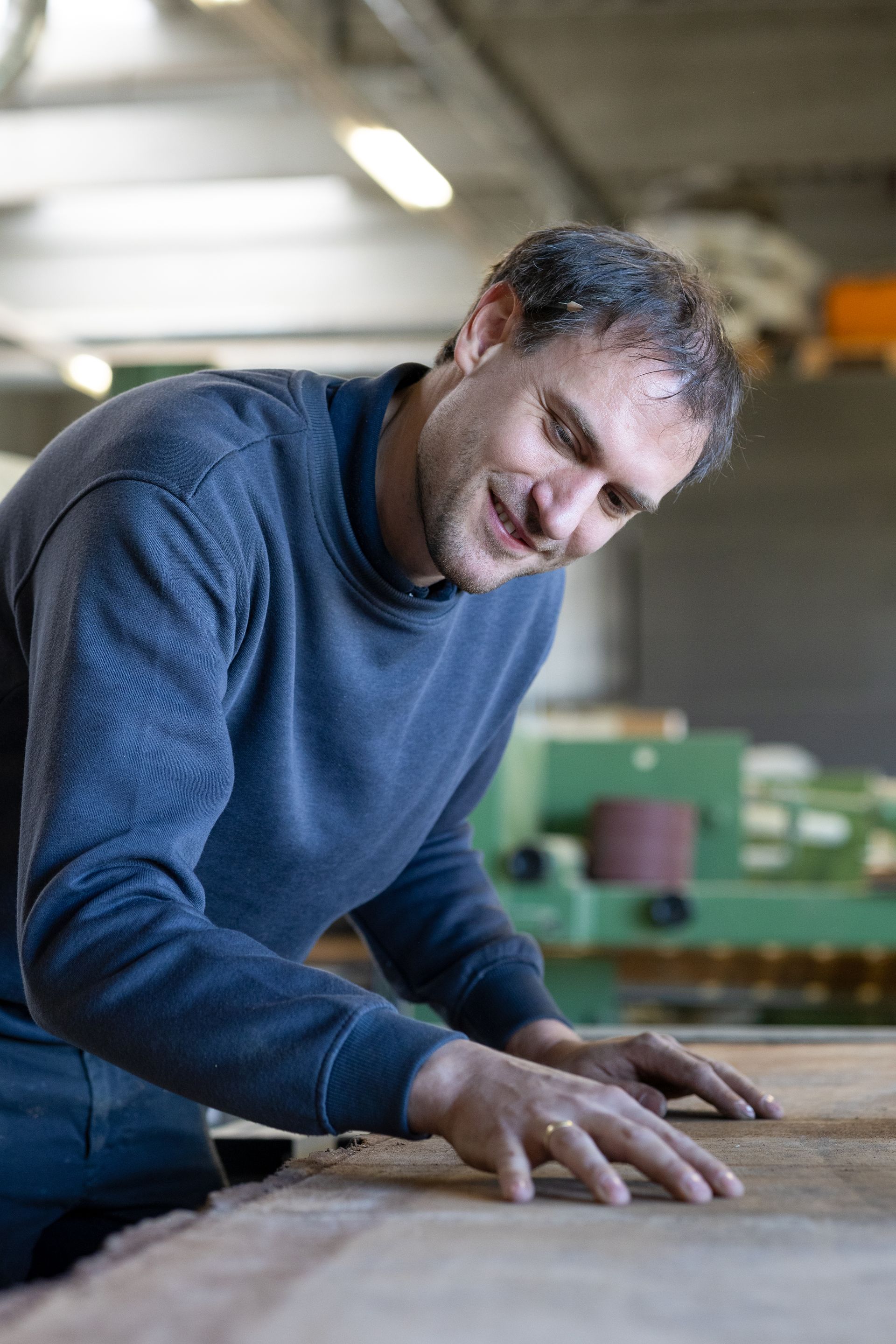 Mann in blauem Pullover beugt sich in einer Werkstatt über eine Holzfläche. Fotograf Tübingen. Fotograf Reutlingen.