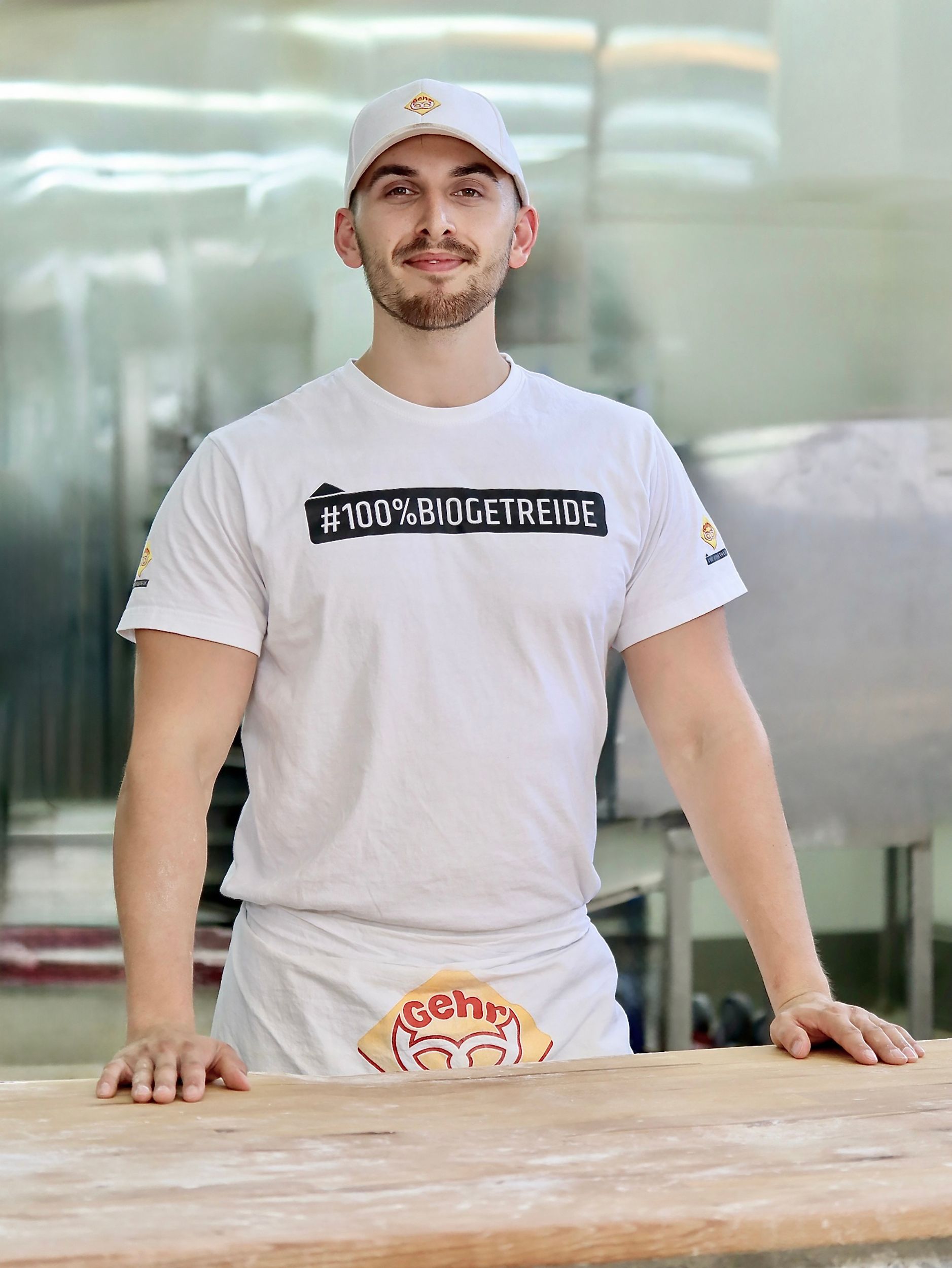 Ein Bäcker in weißer Uniform steht hinter einem hölzernen Tresen in einer Bäckerei. Fotograf Tübingen. Fotograf Reutlingen.