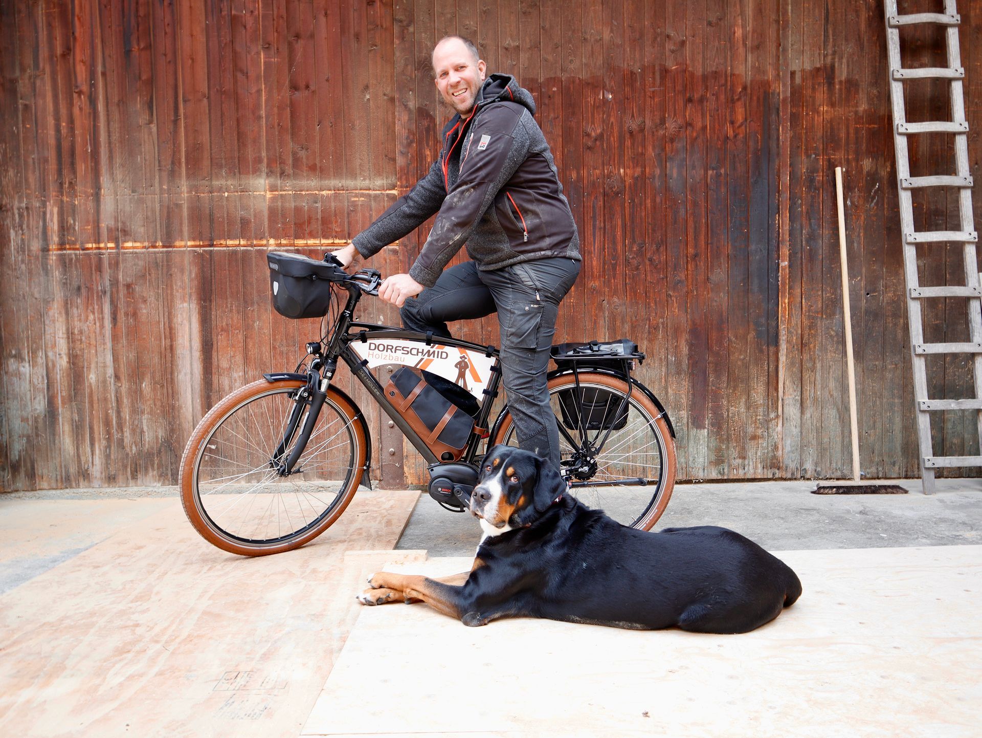 Mann auf Fahrrad lächelt, Hund ruht sich aus. Kulisse: rostige Metallscheune.Fotograf Tübingen. Fotograf Reutlingen.