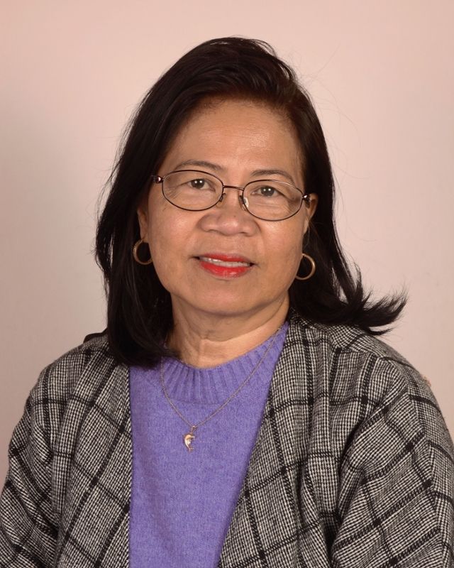 A woman wearing glasses and a purple sweater is smiling for the camera.