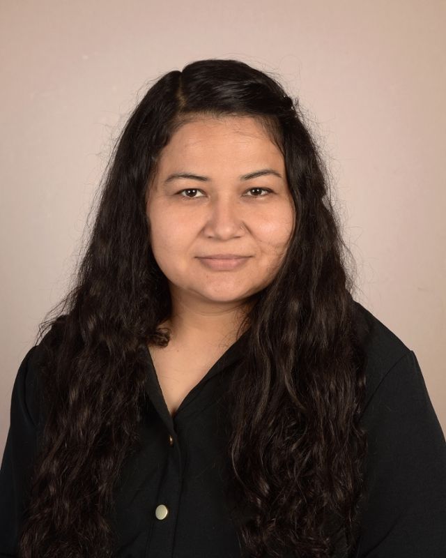 A woman with long dark hair is wearing a black shirt and smiling for the camera.